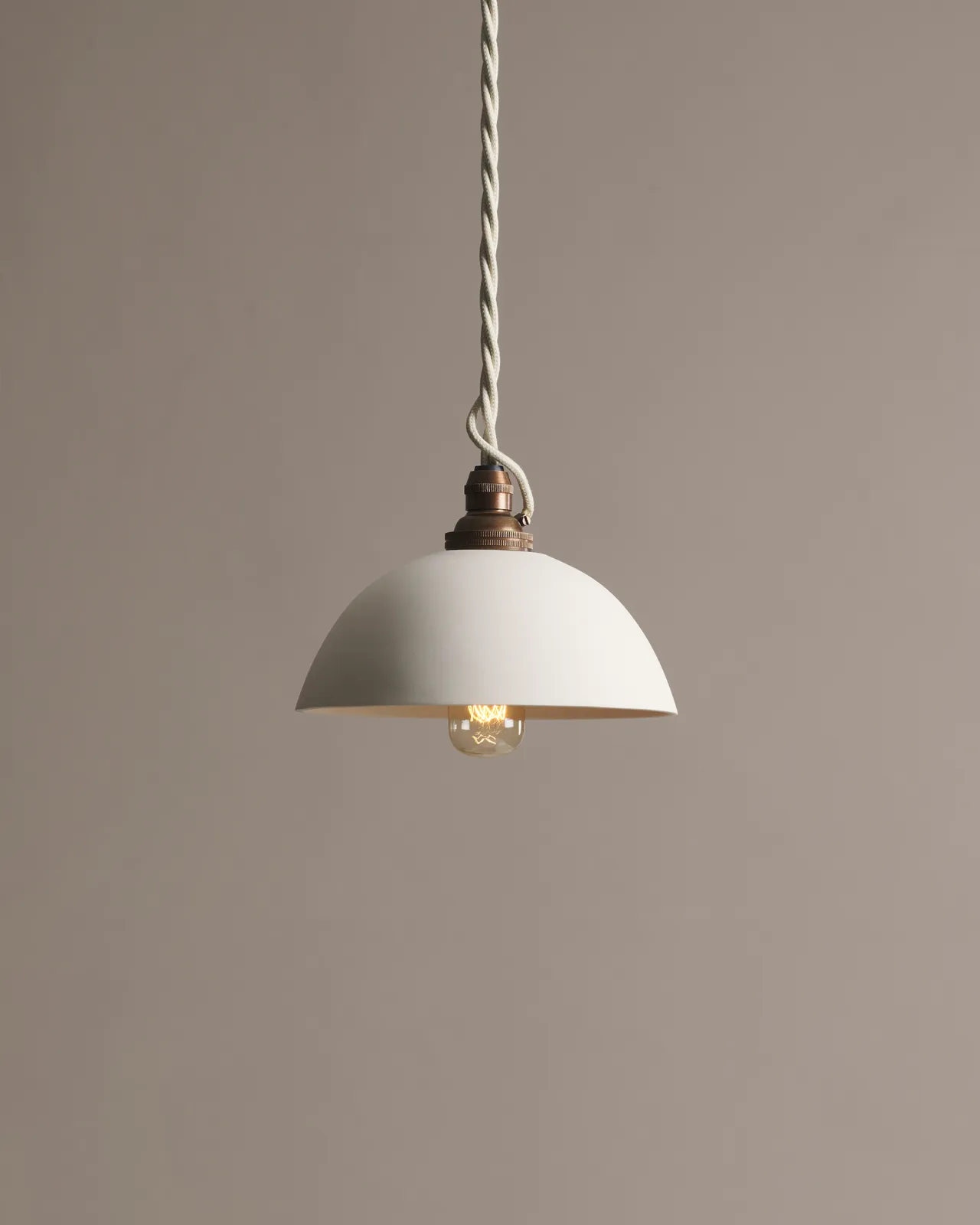 A plain rice bowl porcelain pendant light with an unglazed finish, an aged brass B22 lampholder and a white twisted fabric flex cord.