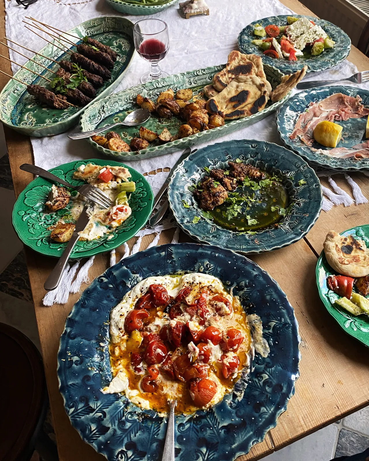 Several oval and round handmade bohemian-style ceramic platters set at a table with a vintage lace tablecloth and a variety of Mediterranean foods.