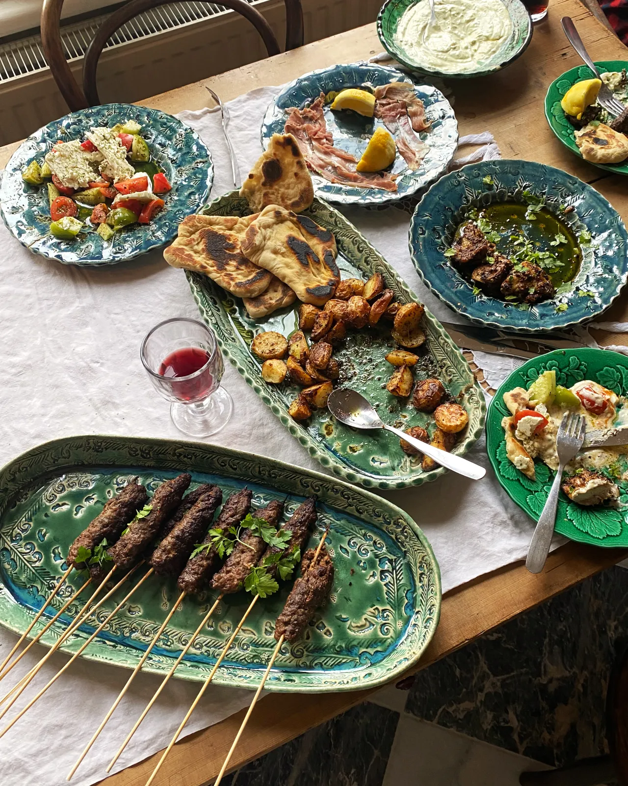 Several oval and round handmade bohemian-style ceramic platters set at a table with a vintage lace tablecloth and a variety of Mediterranean foods.