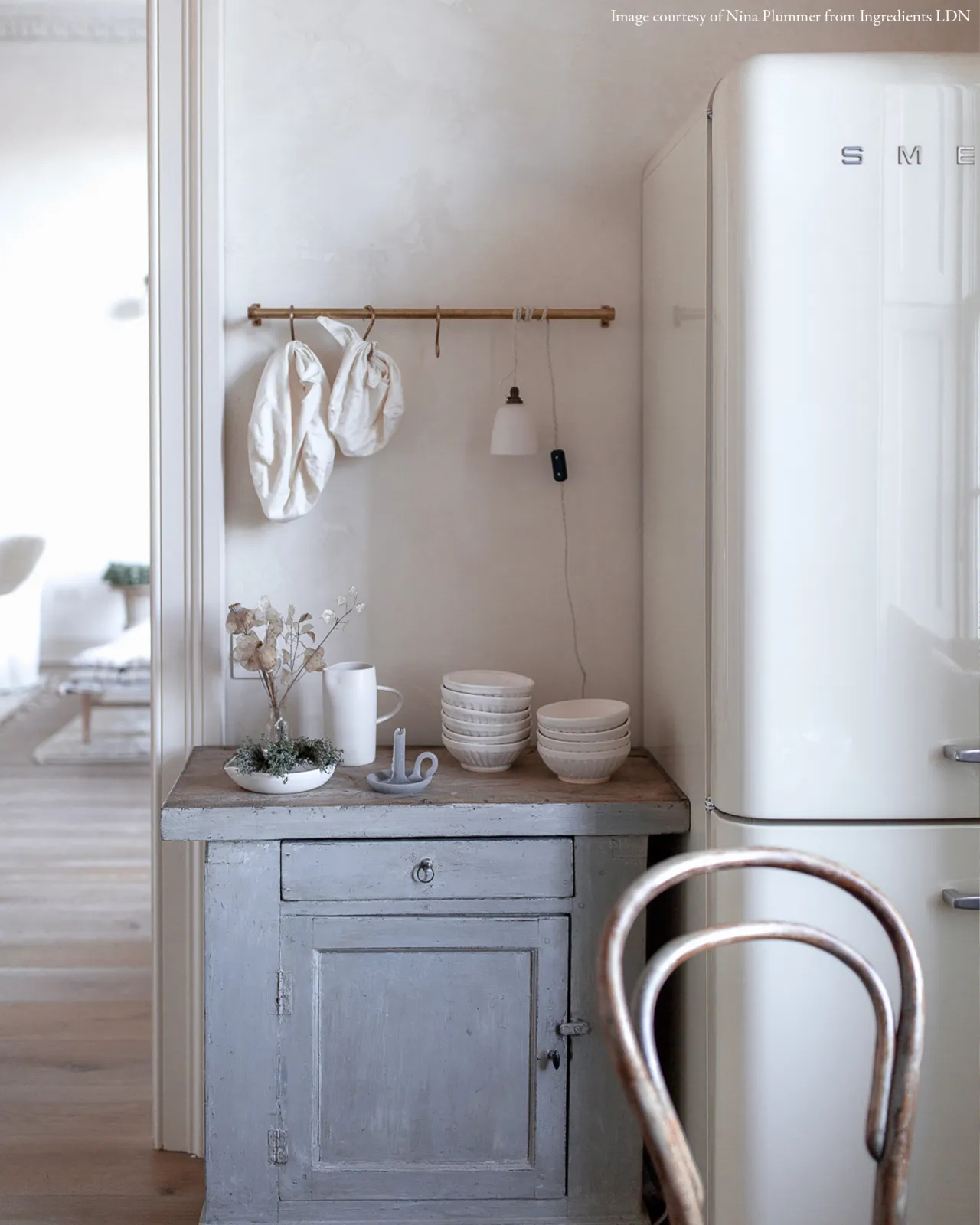 A plain beaker porcelain plug-in light hanging a short aged brass hanging rail beside a large white fridge/freezer.