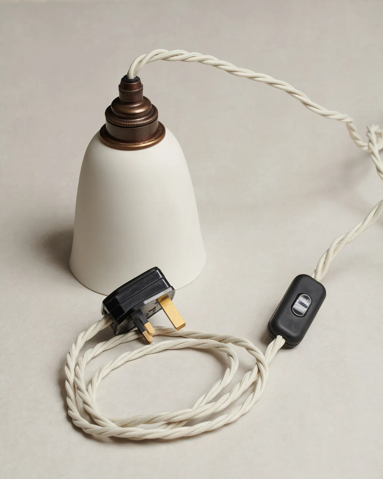 A large plain beaker porcelain plug-in light with an unglazed finish, white twisted fabric flex cord, brass fittings and a black plastic switch and plug.