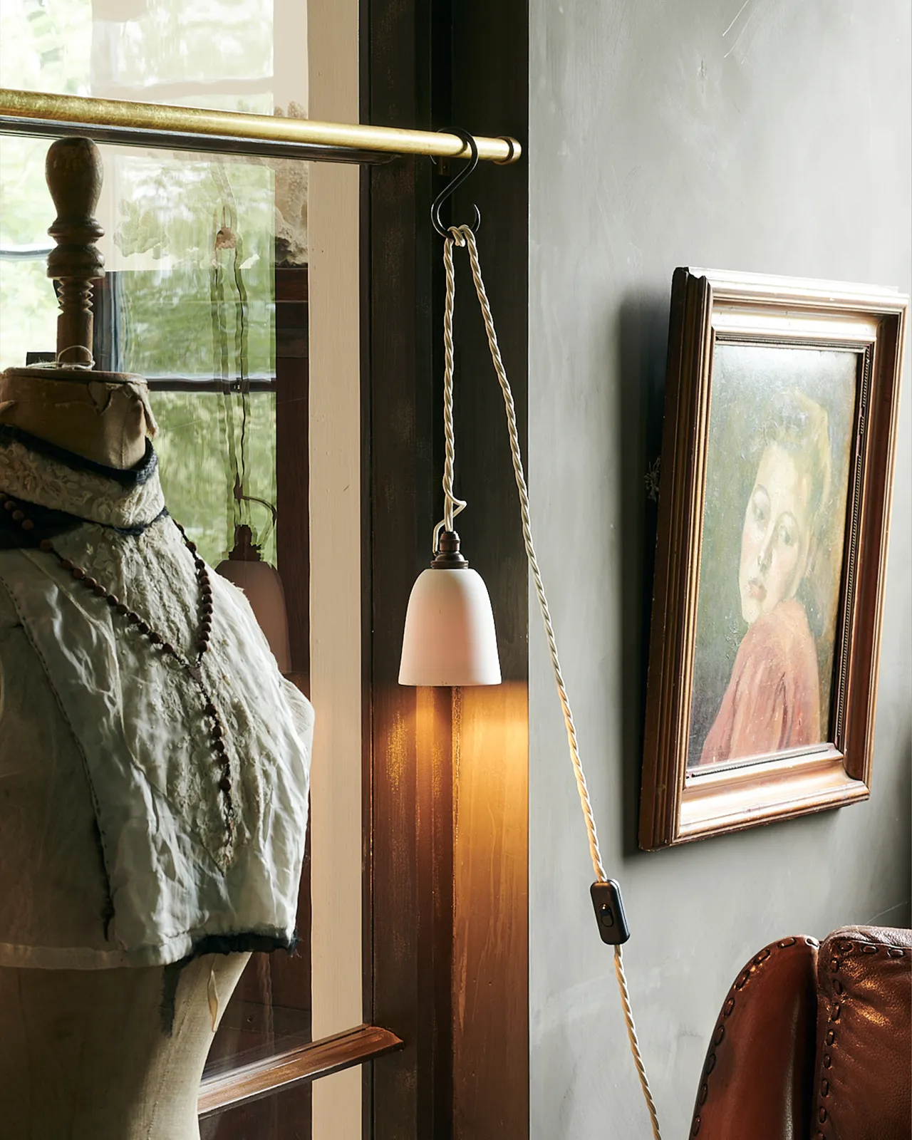 A plain beaker porcelain plug-in light hanging from wooden ladder beside a mid-century-style glazed pantry cupboard.