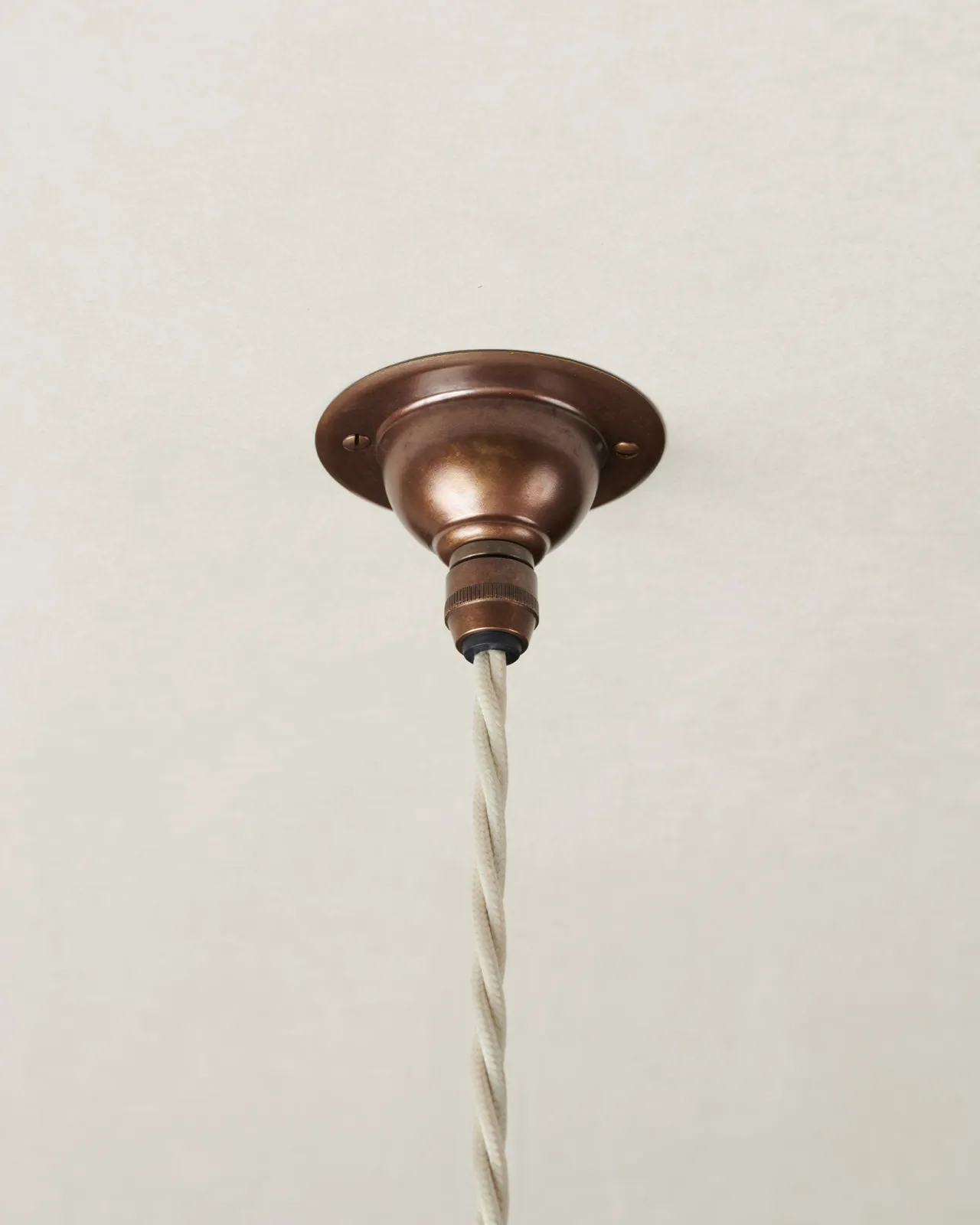 A small aged brass ceiling rose with a white twisted fabric flex cord.
