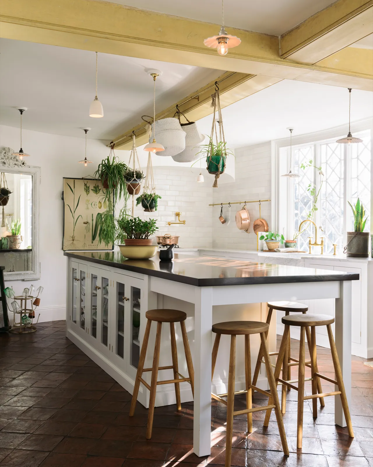 A Mediterranean-style kitchen with white painted cabinetry, white walls, terracotta flooring and an assortment of unglazed porcelain pendant lights hanging at various heights.
