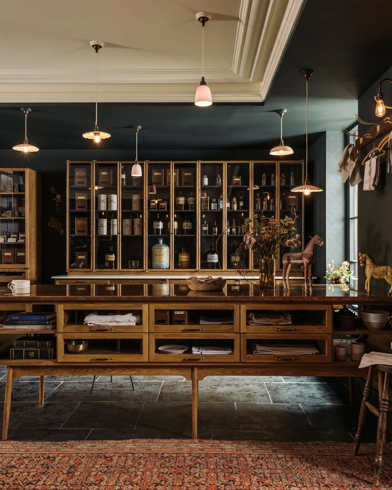 A straight-on view of a mid-century-style kitchen with oak cabinetry, dark painted walls and an assortment of unglazed porcelain pendant lights hanging at various heights.