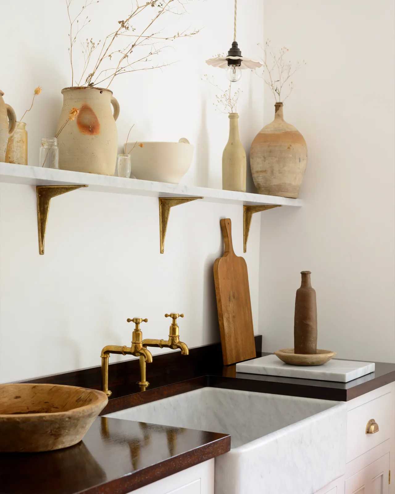 An oblique view of a small pleated porcelain light hanging over a Carrara marble sink.