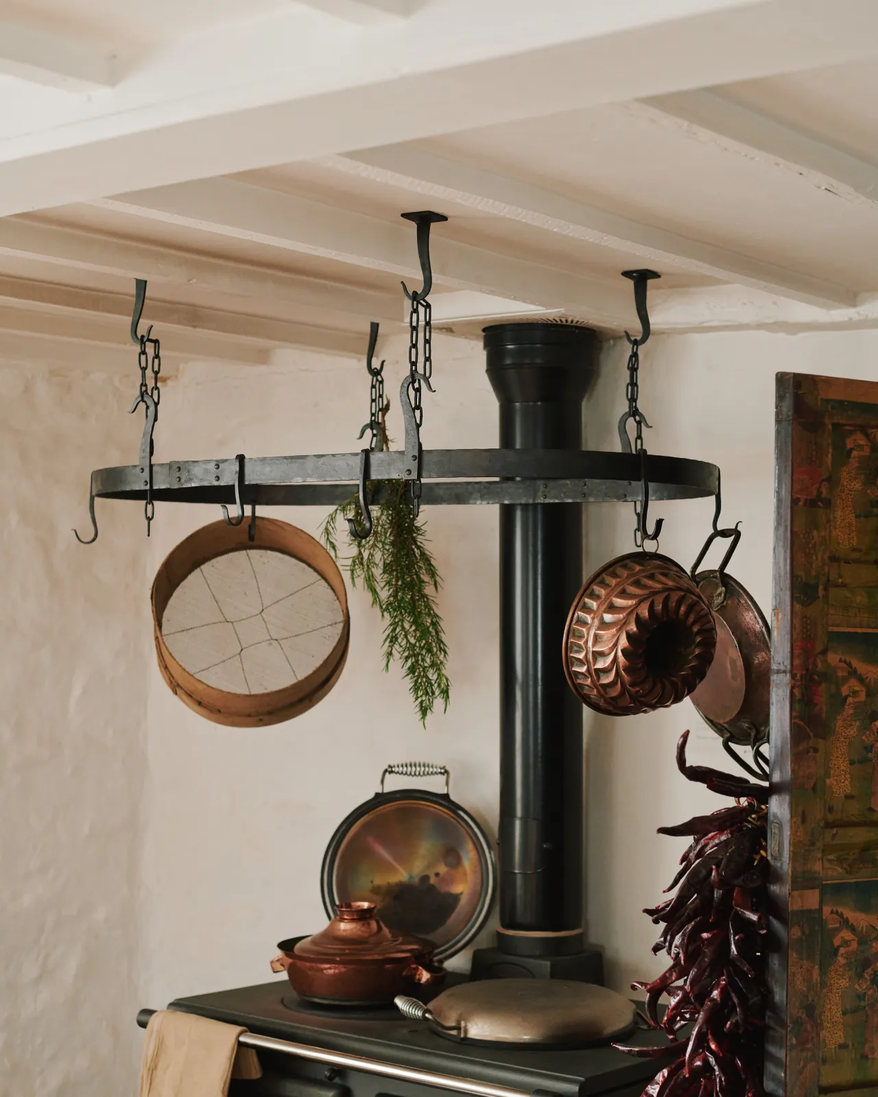 An oblique view of a large oval-shaped wrought iron pot hanger suspended from chains above a black stove cooker.