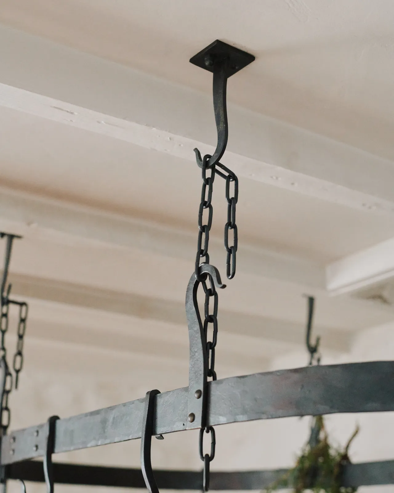A close-up view of a black chain between the hooks of a wrought iron pot hanger.