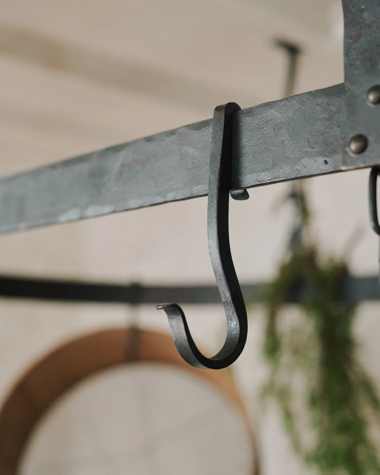 A close-up view of a looped wrought iron hook hanging from the frame of a large oval-shaped pot hanger.