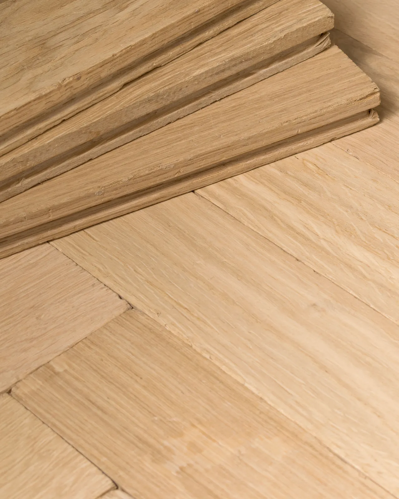 A close-up view of oak parquet flooring with a light natural finish. Three loose blocks are stacked in one corner.