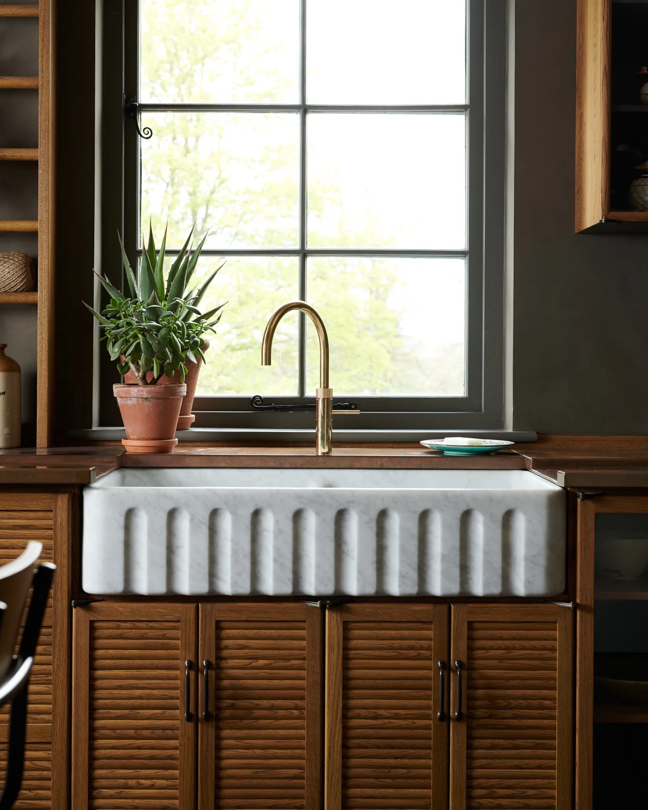A contemporary-style brass tap in a mid-century-style kitchen with oak cupboard doors, a fluted Carrara marble sink and an aged copper worktop.