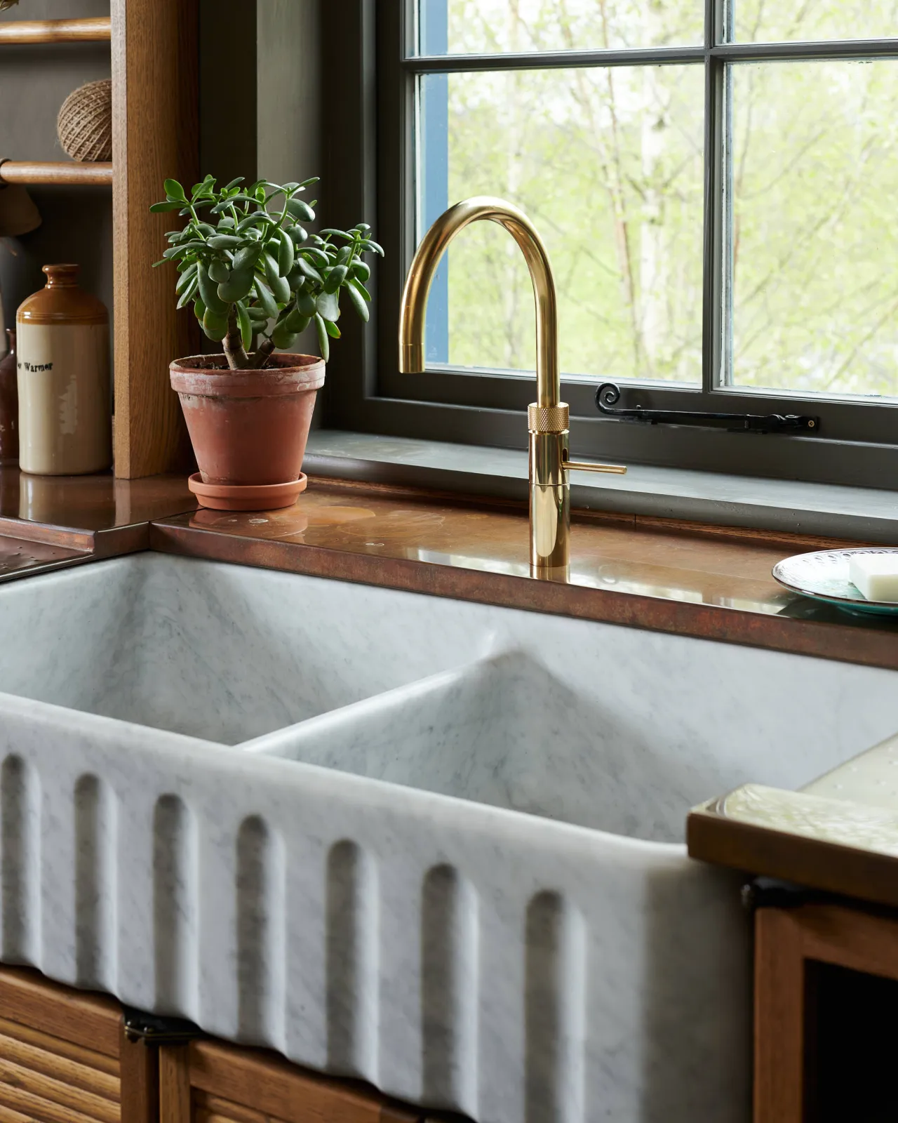A contemporary-style brass tap above a grand fluted double bowl Carrara marble sink and an aged copper worktop.