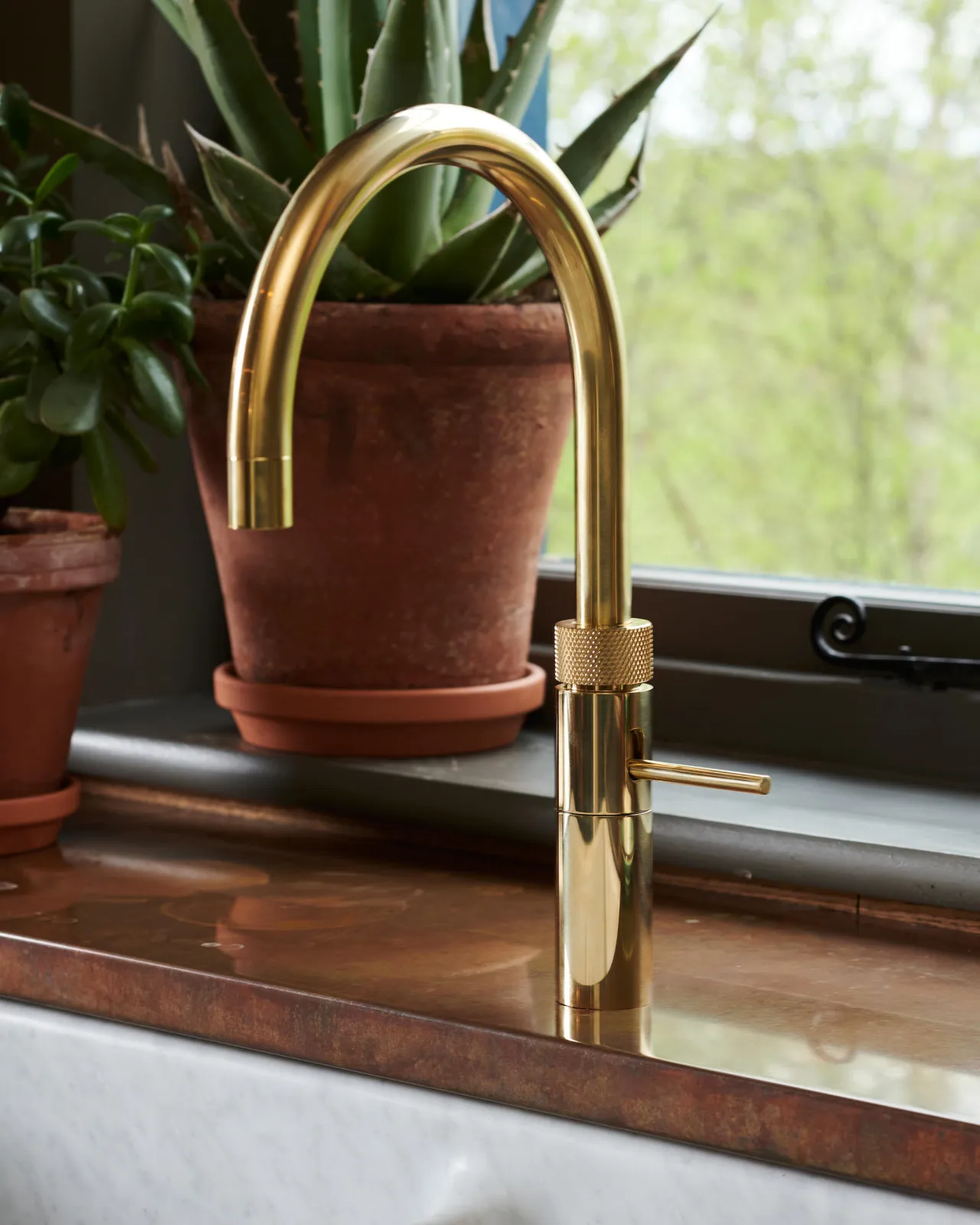 A contemporary-style brass tap with a small lever handle and a minimal design on an aged copper worktop.