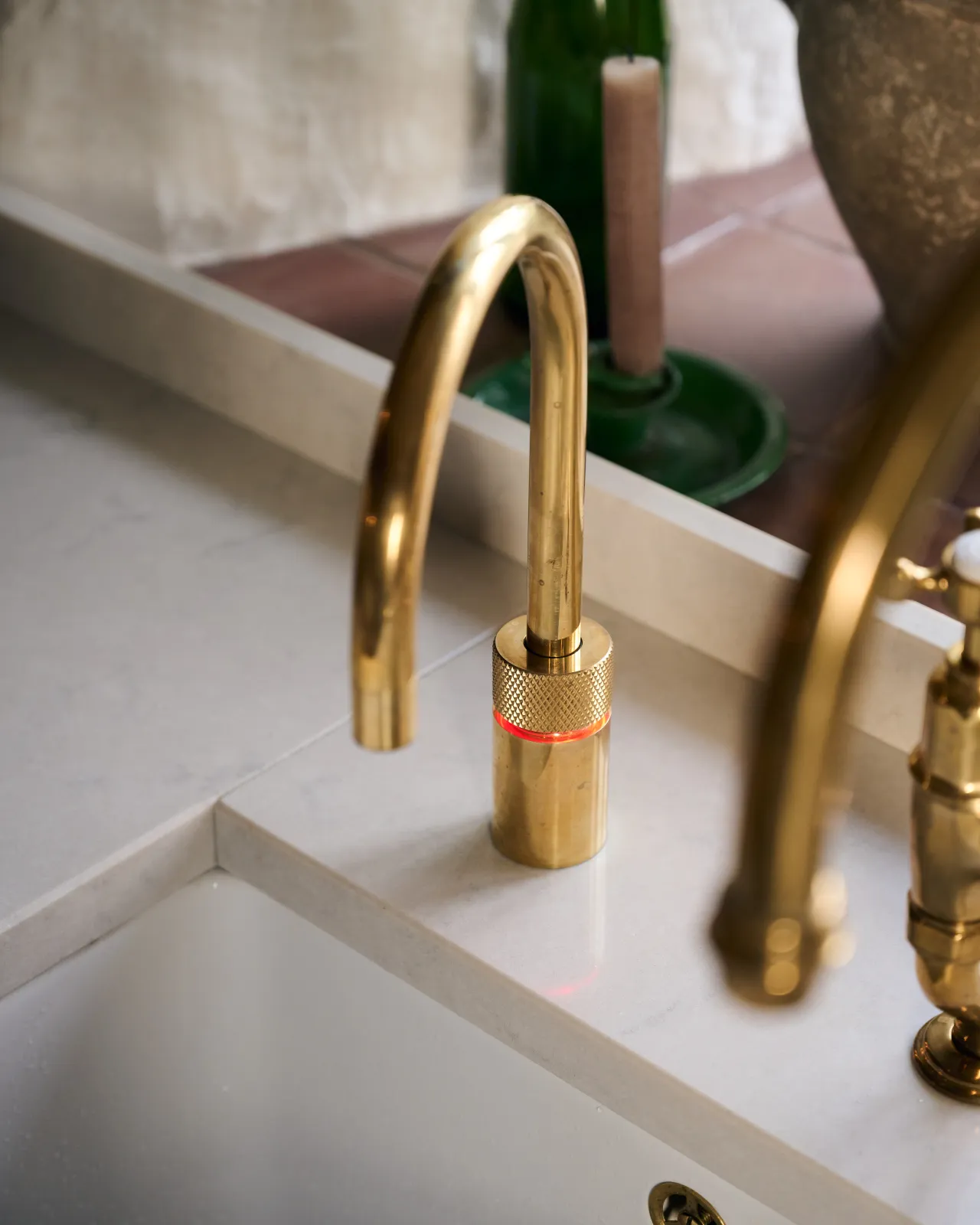 A contemporary-style brass tap seen from above, a ring of red light can be seen emanating from under a knurled cuff.