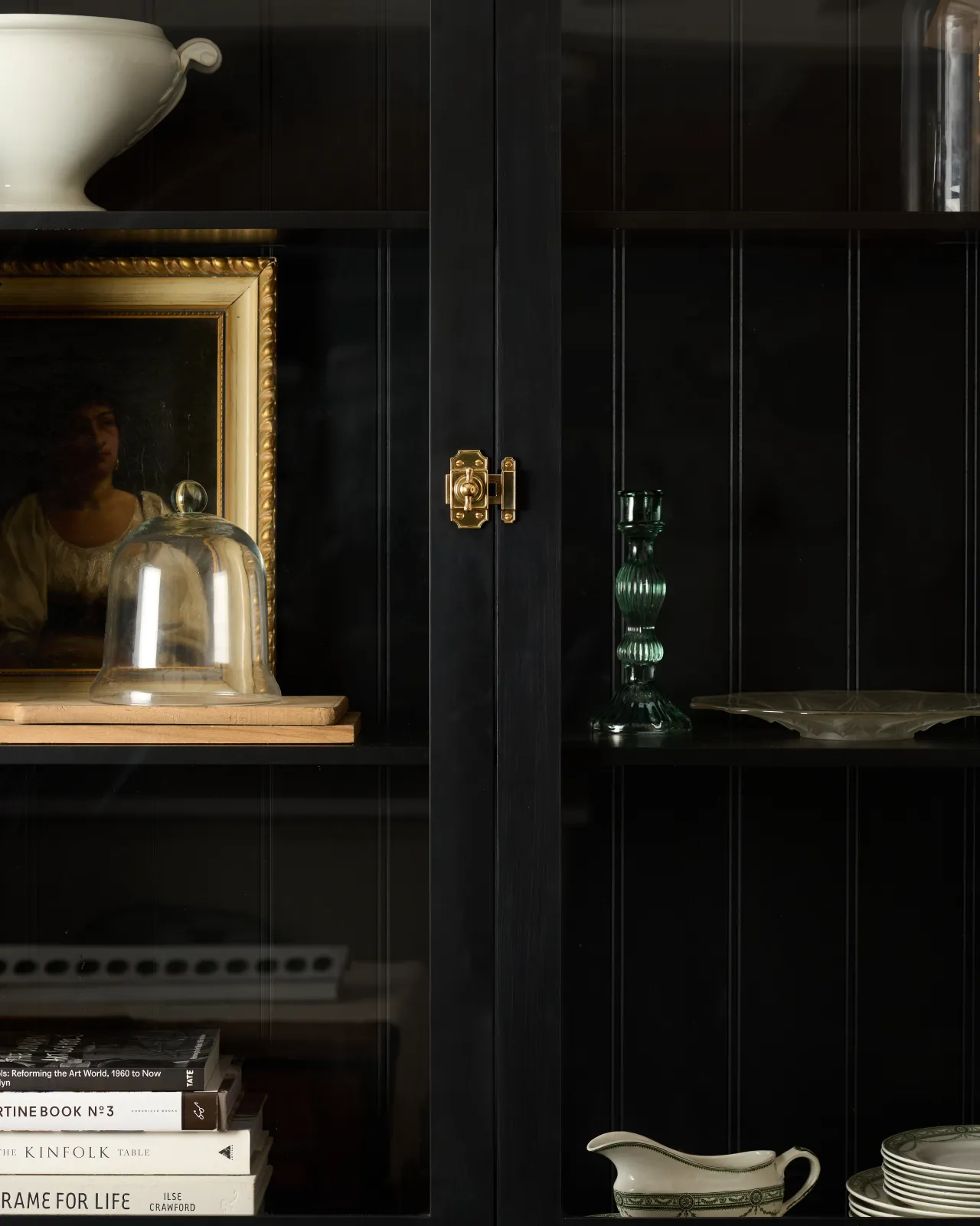A straight-on view of a Victorian-inspired rack and pinion cupboard catch in a warm burnished brass finish, fitted to a tall glazed cupboard painted black inside and out.