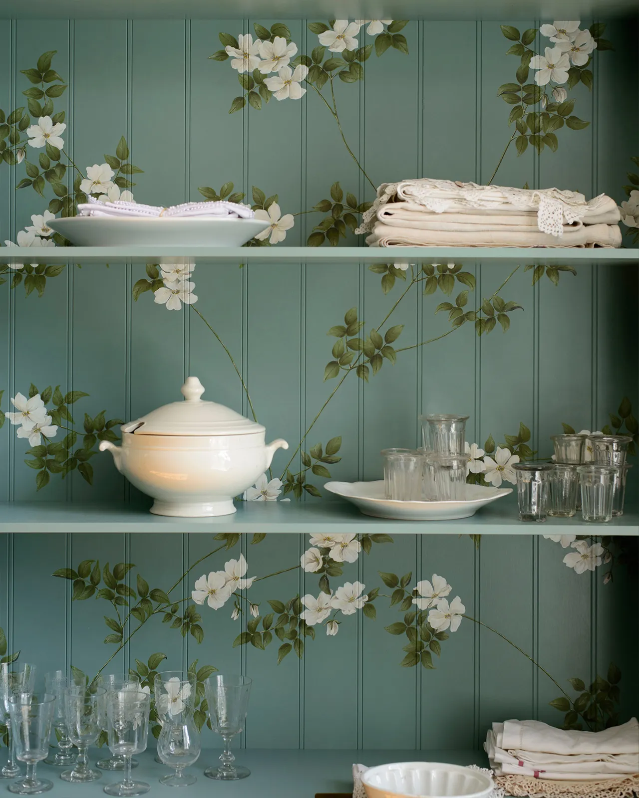 The interior of a display cabinet with a duck-egg blue interior and painted flowing white dog-roses on the tongue and groove back panel.
