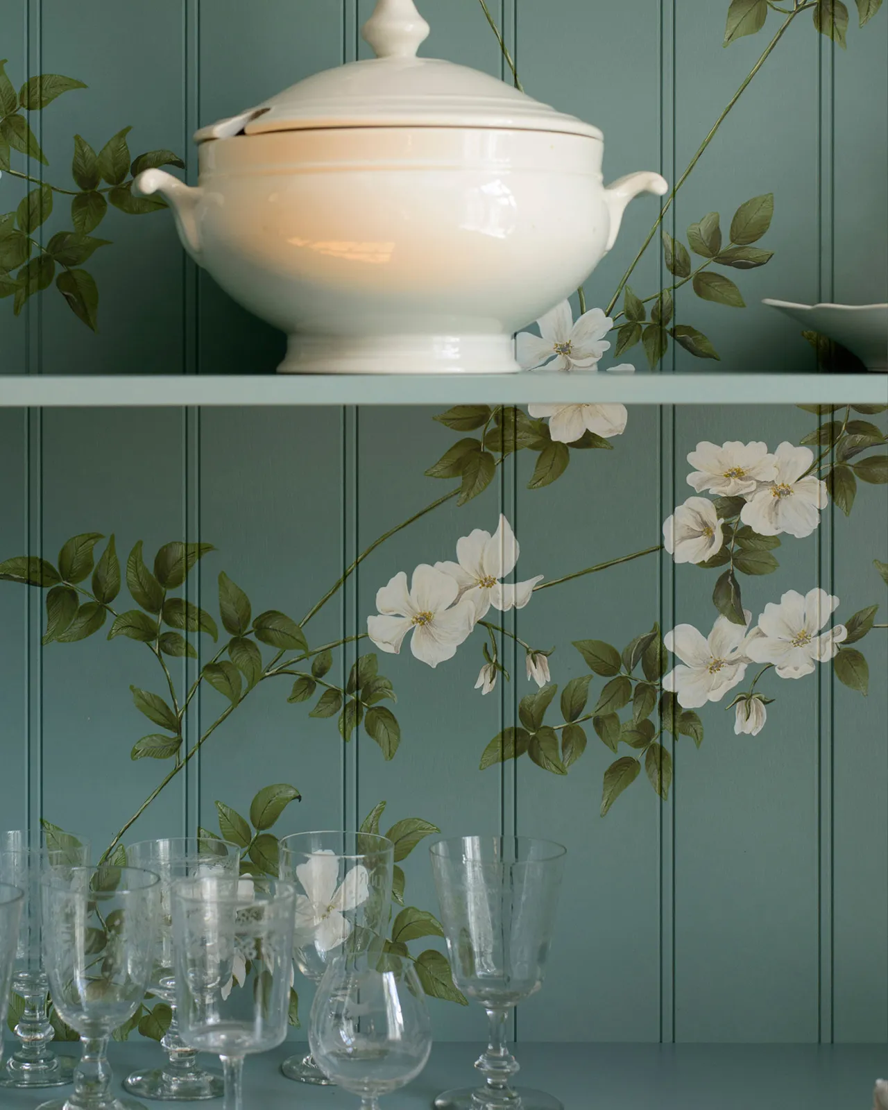 A close-up view of painted flowing white dog-roses on the tongue and groove back panel. A large white dish sits on a shelf above.