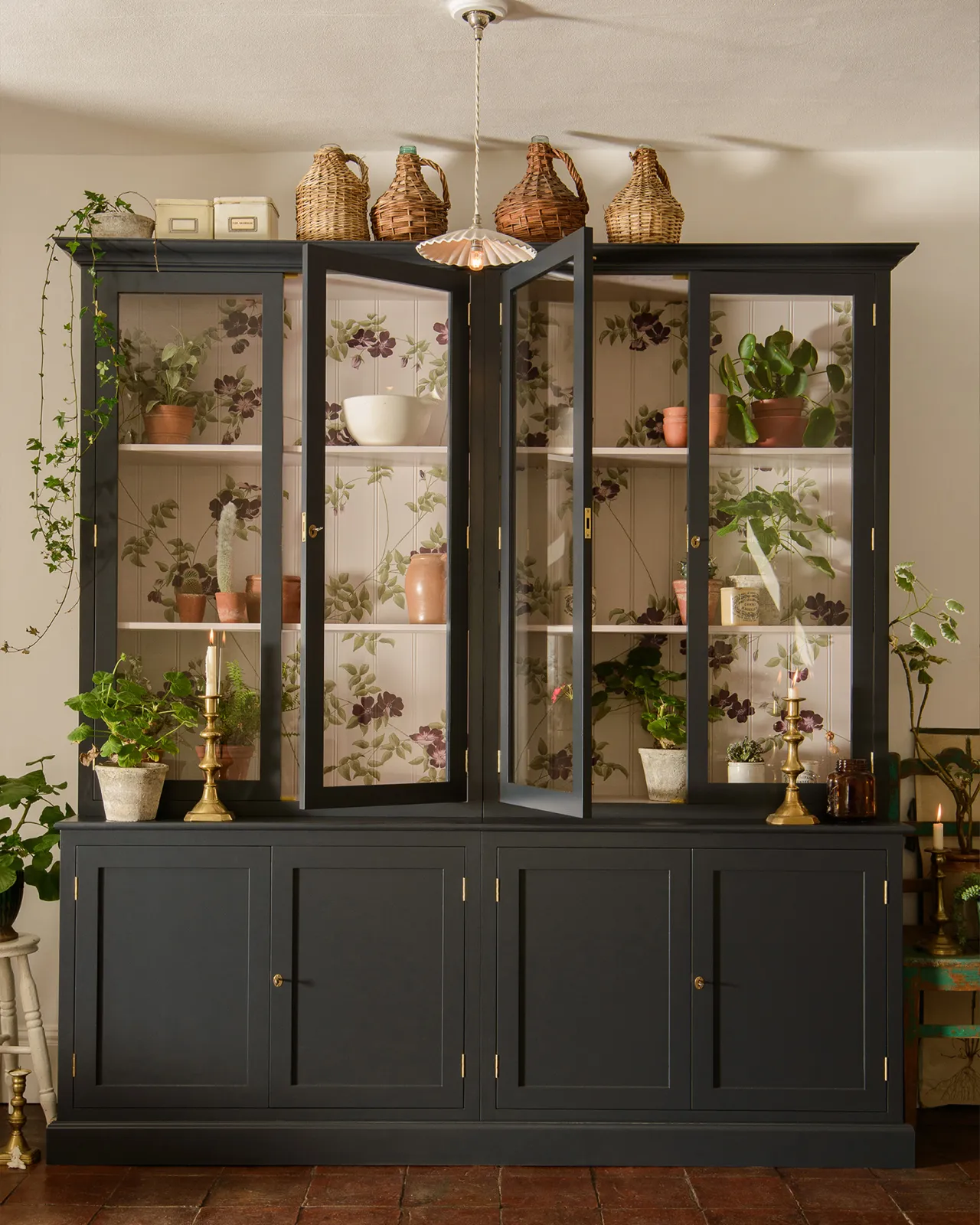 A tall double museum-style display cabinet with glazed doors, painted a dark blue outside with a light pink interior and painted flowing purple dog-roses on the tongue and groove back panel.