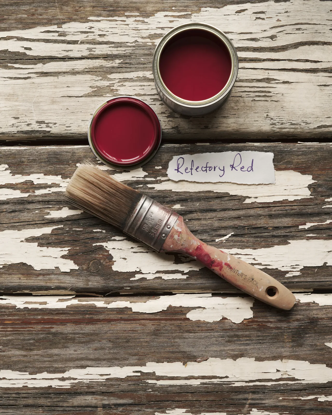 An overhead view of an open paint pot and a worn brush on a rustic tabletop. The rich red colour inside is labelled 'Refectory Red'.
