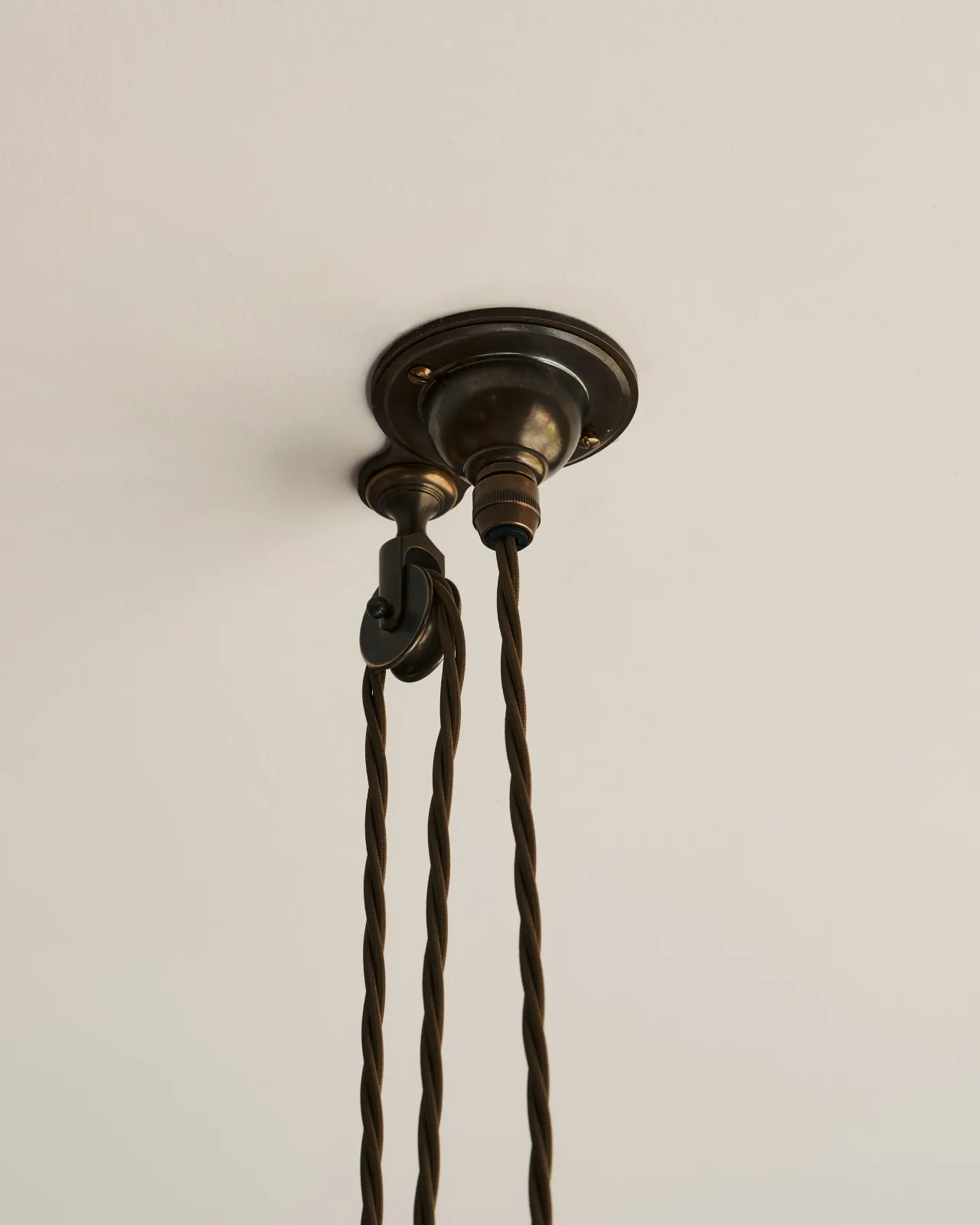 A small aged brass ceiling rose with a wheel pulley and a brown twisted fabric flex cord.