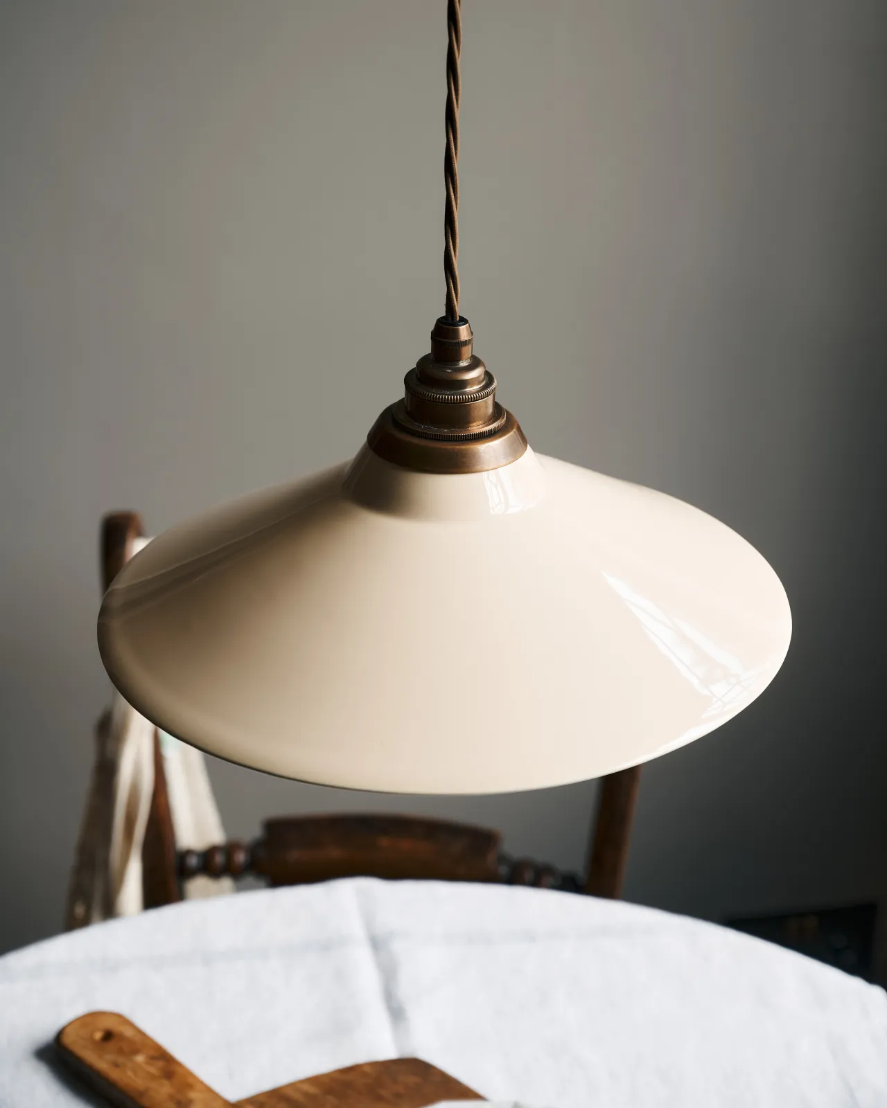 A close-up view of a small cream glazed ceramic shade with aged brass fittings and brown twisted fabric flex cord.