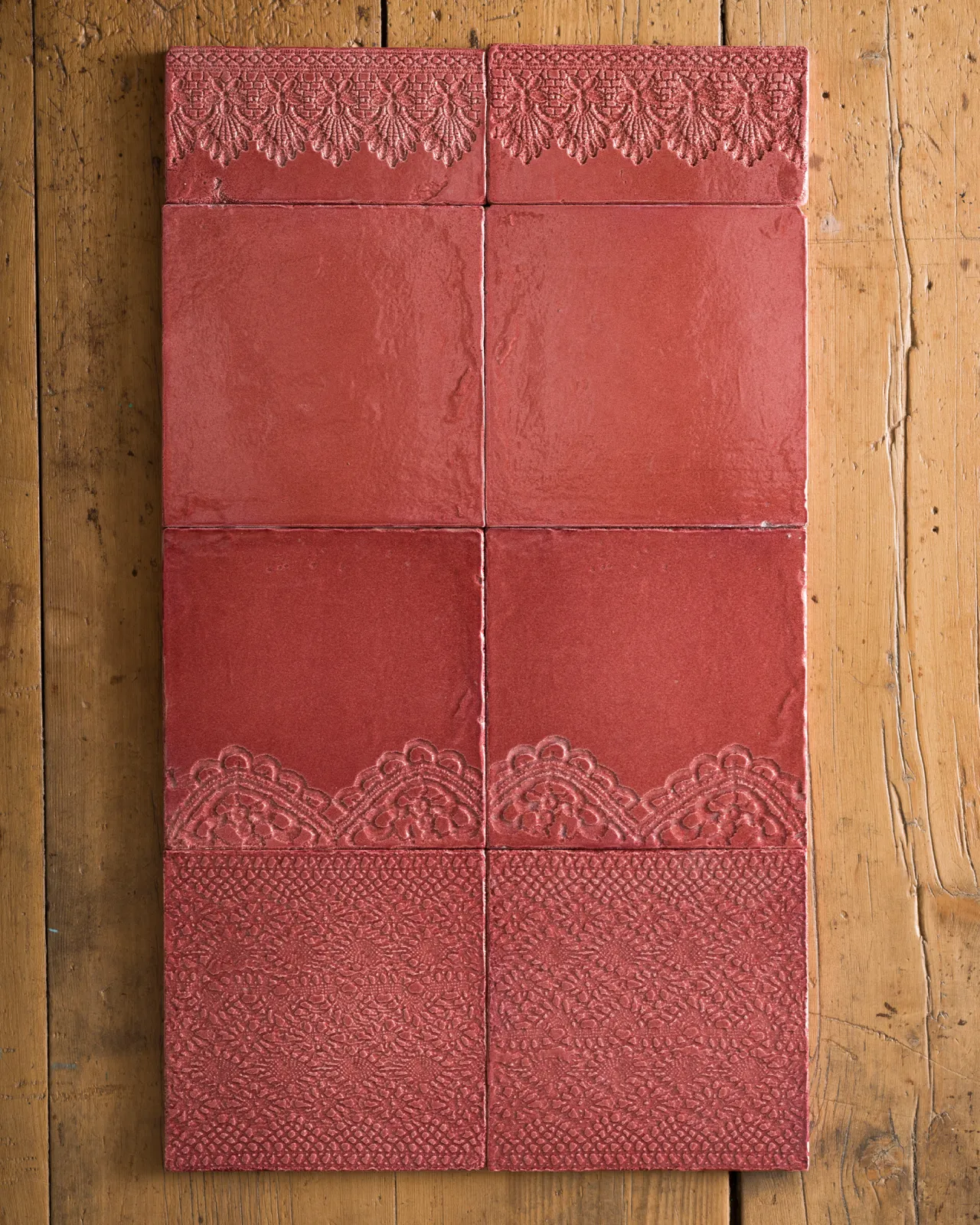 A small arrangement of handmade glossy rose wall tiles - some plain, some with decorative lace patterns - on an old wooden tabletop.
