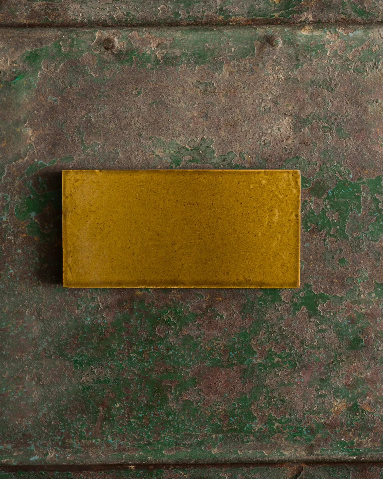 A glossy sepia metro tile on a rustic metallic surface.