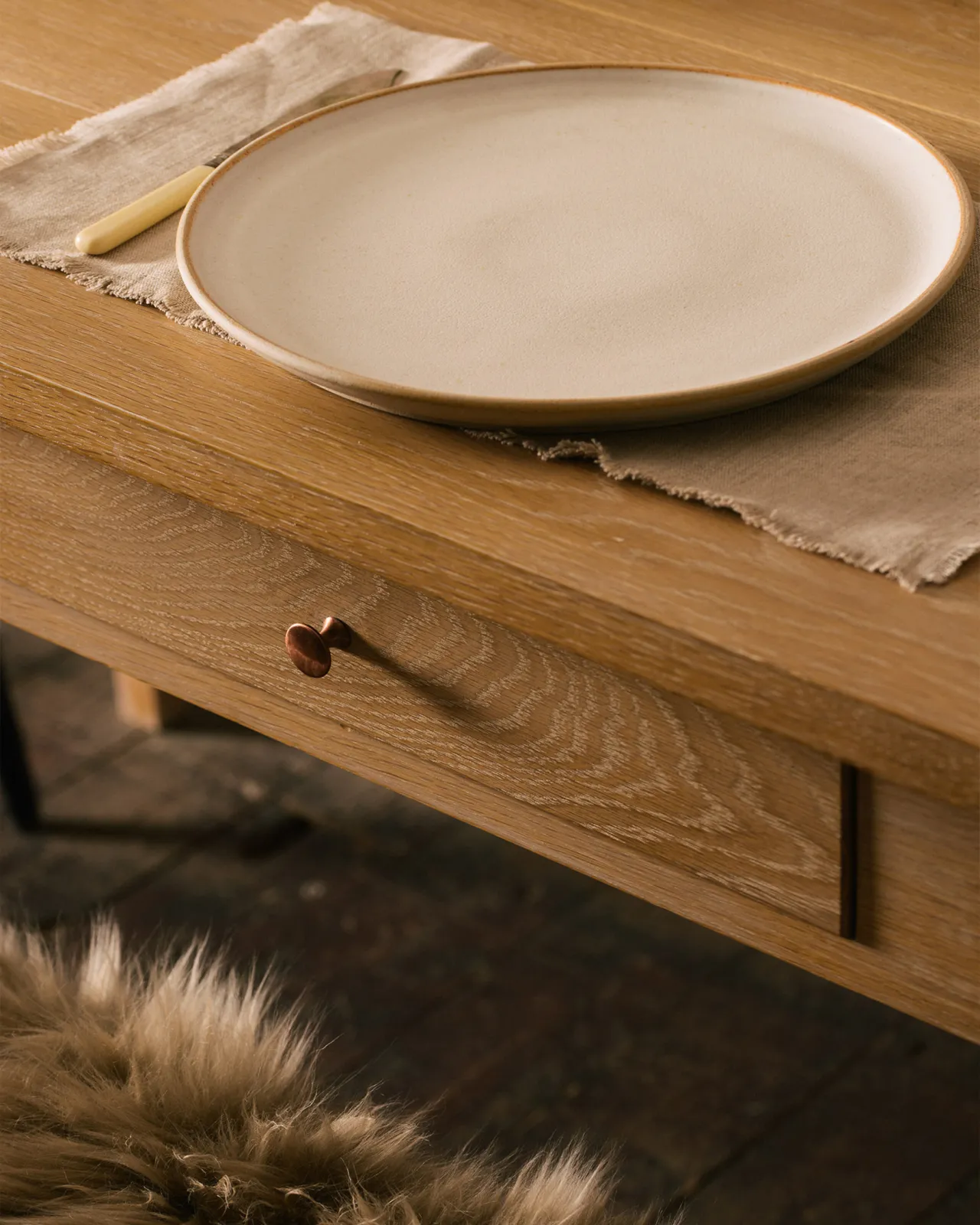A close-up view of a shallow drawer in the apron of a Shaker-style oak dining table.