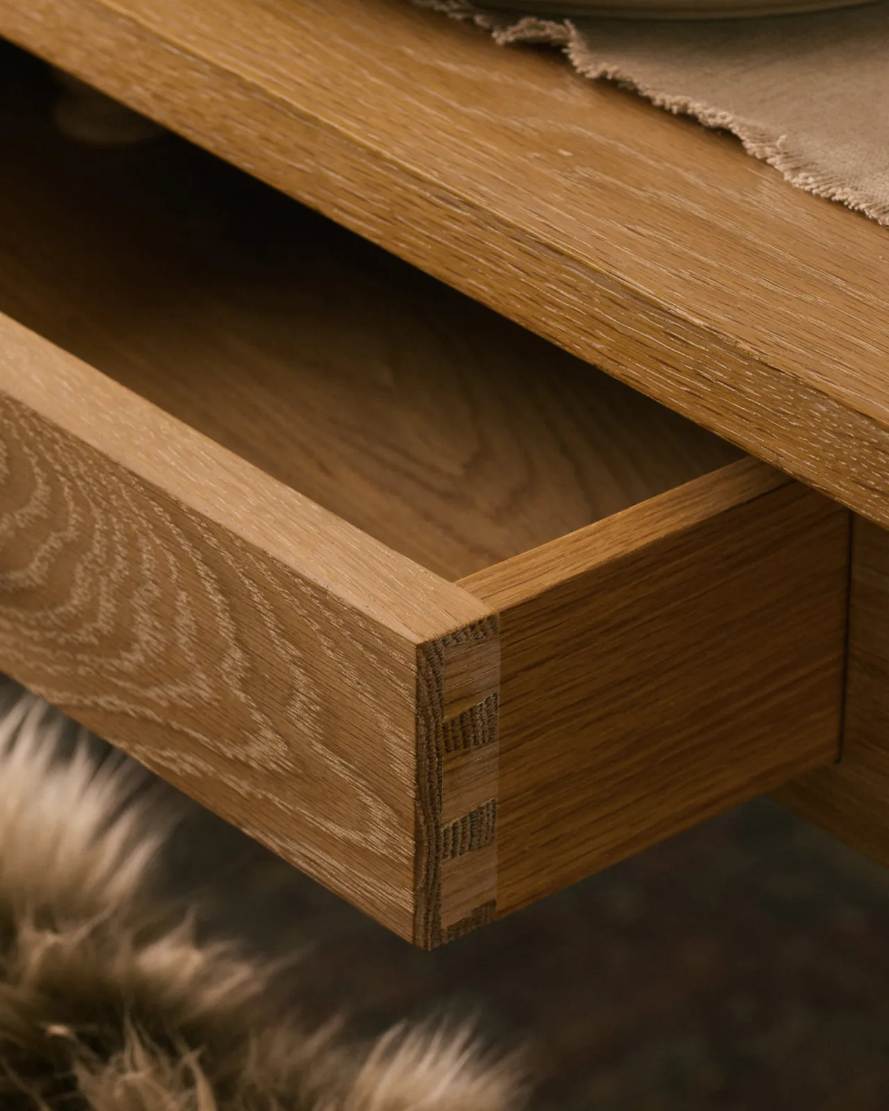 A close-up view of an open shallow drawer with dovetailed joinery in the apron of a Shaker-style oak dining table.