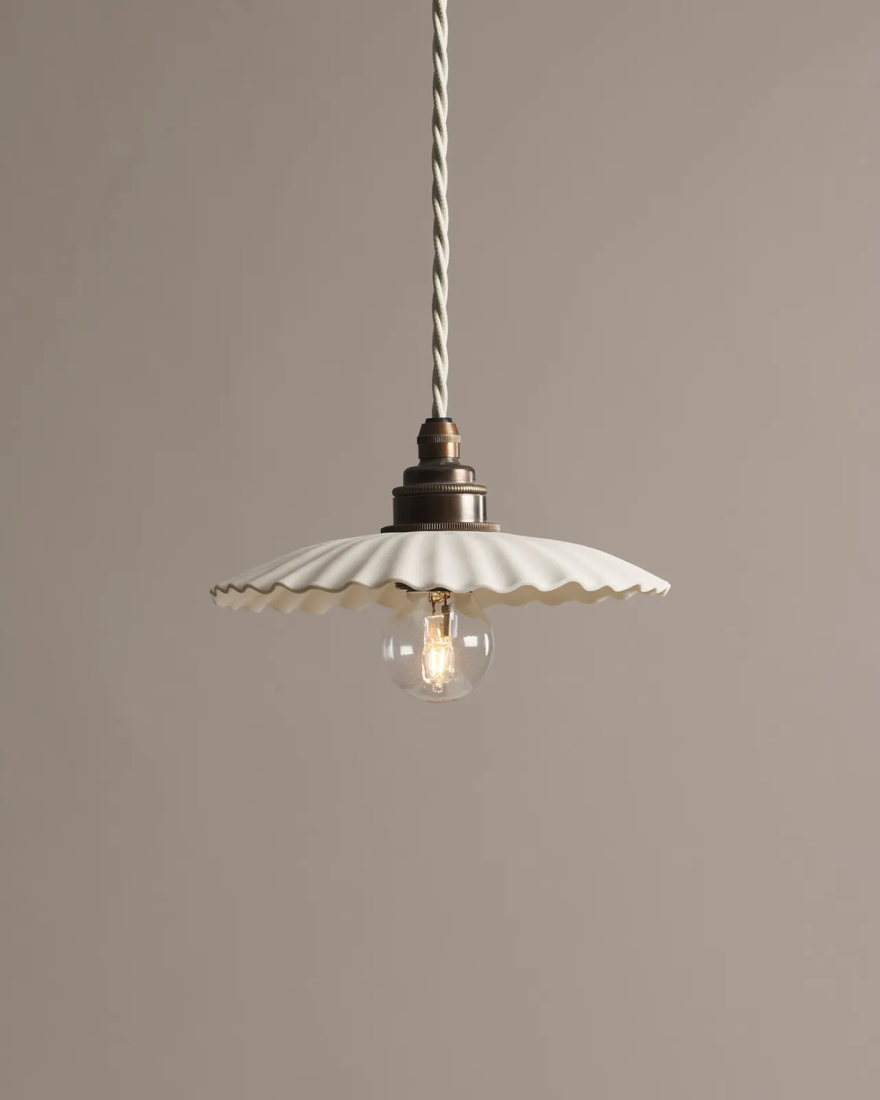 A small narrow pleat porcelain pendant light with an unglazed finish, an aged brass E27 lampholder and a white twisted fabric flex cord.