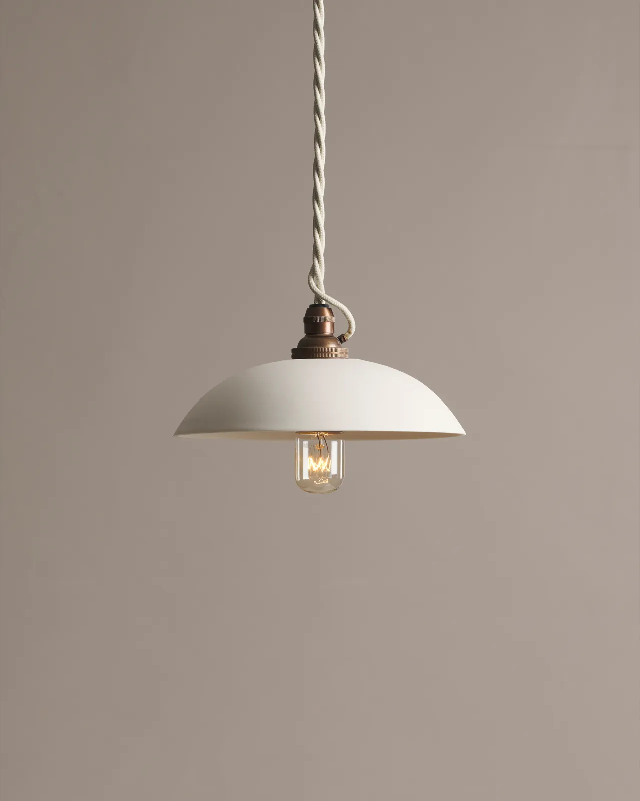 A small plain skullcap porcelain pendant light with an unglazed finish, an aged brass E27 lampholder and a white twisted fabric flex cord.