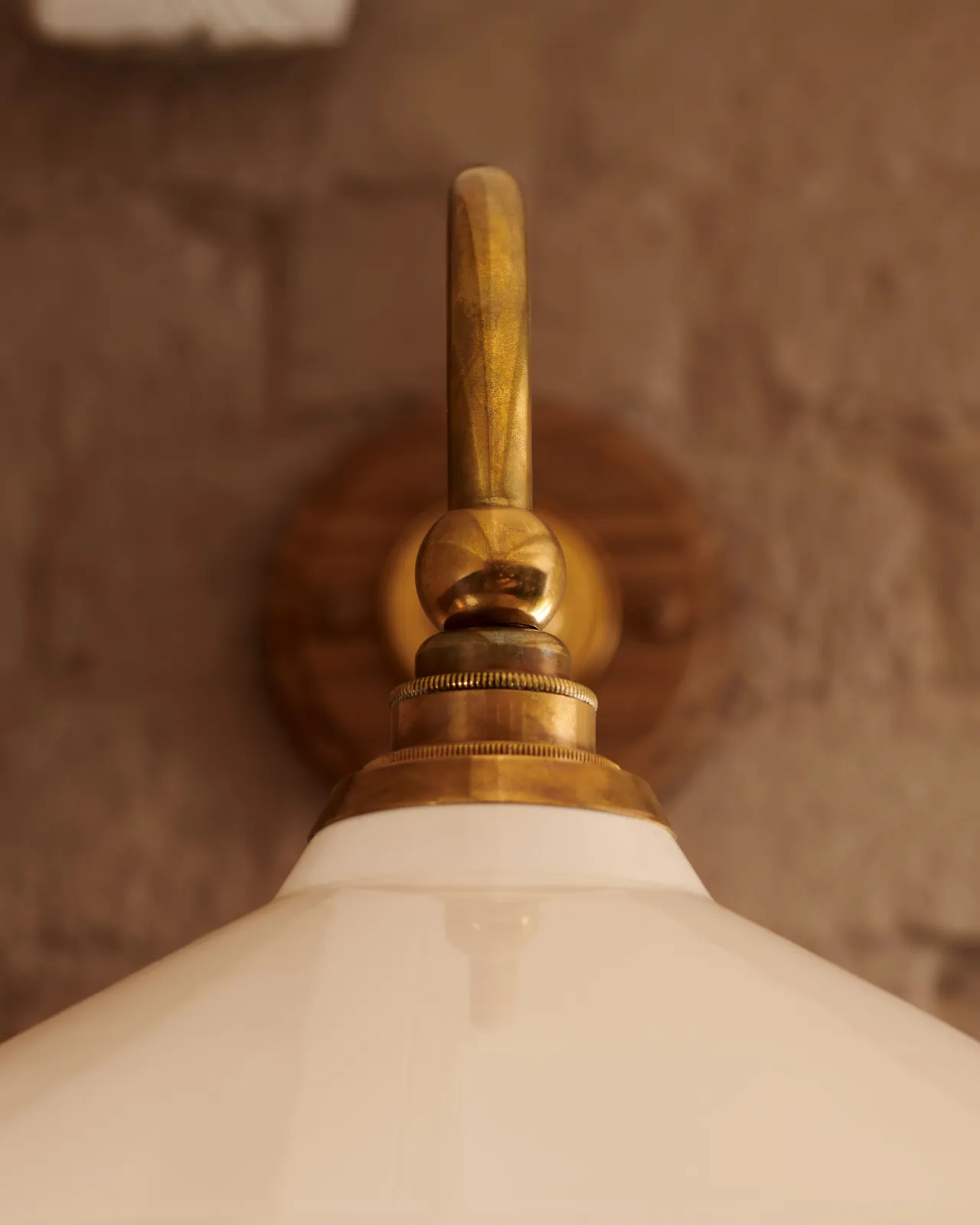 A close-up front profile view of the brass arm and cuff of a Victorian-inspired wall light with a cream glazed ceramic shade.