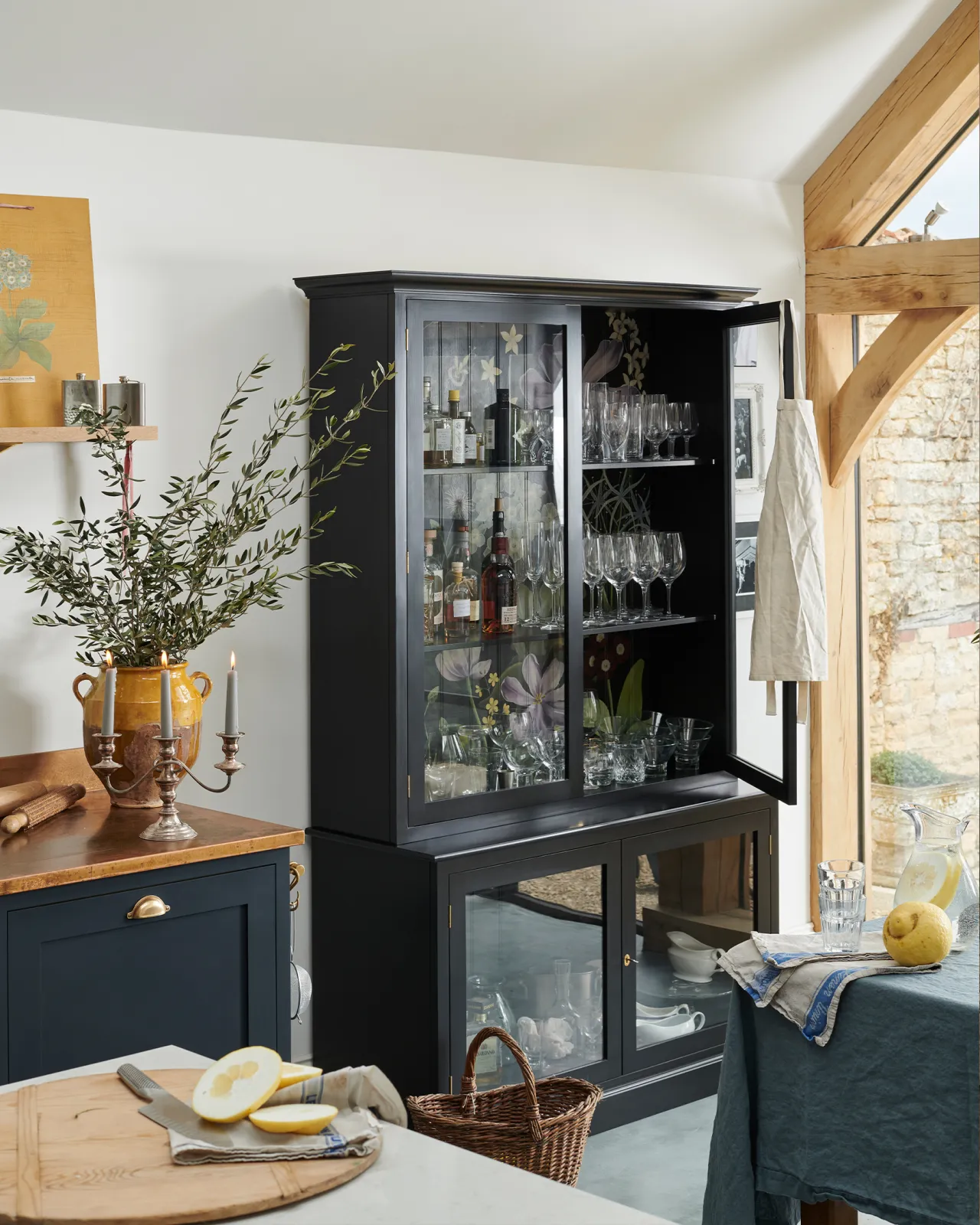 An oblique view of a tall museum-style display cabinet with glazed doors, painted black inside and out and with an elegant and bustling painted floral design on the tongue and groove back panel.