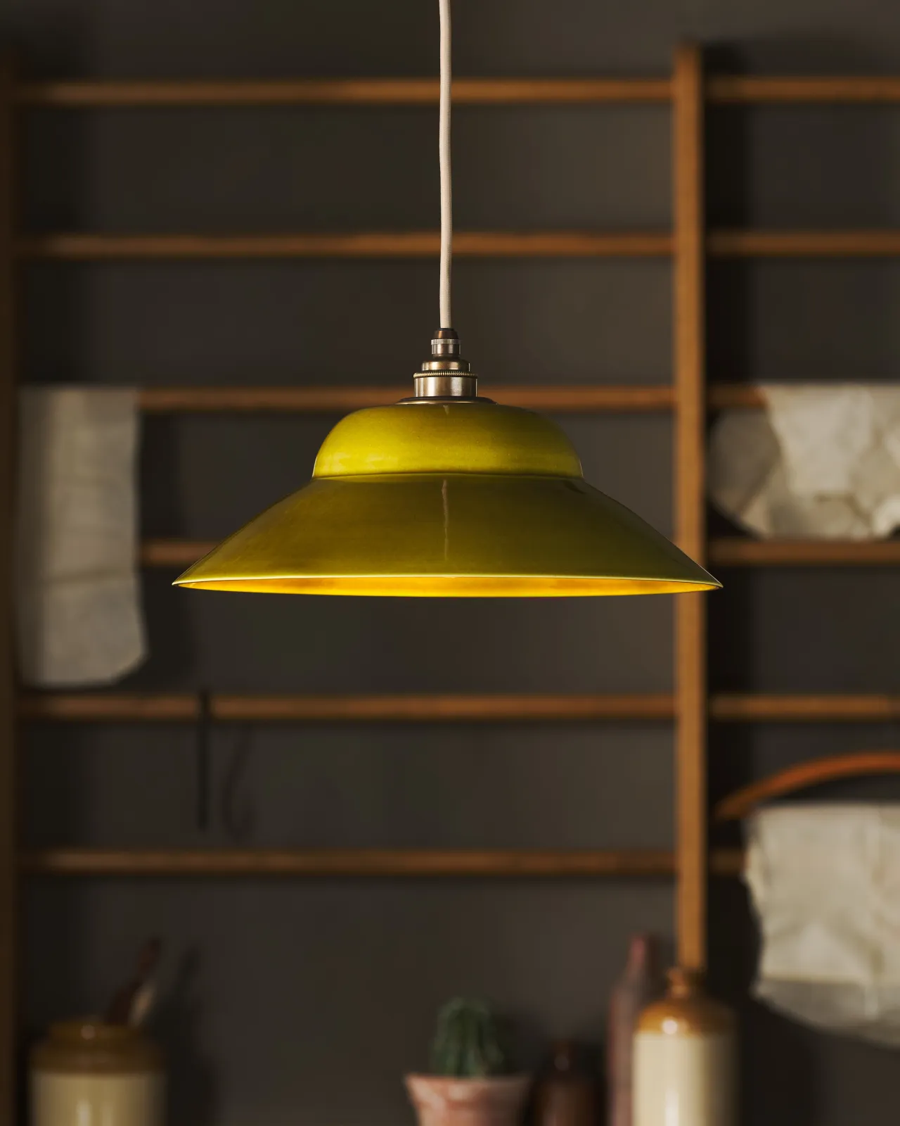 A straight-on view of a mid-century-style chartreuse glazed ceramic pendant light in front of oak racking.