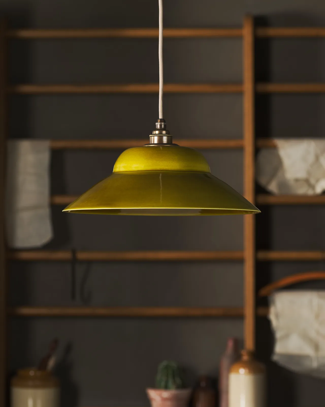 A straight-on view of a mid-century-style chartreuse glazed ceramic pendant light in front of oak racking.