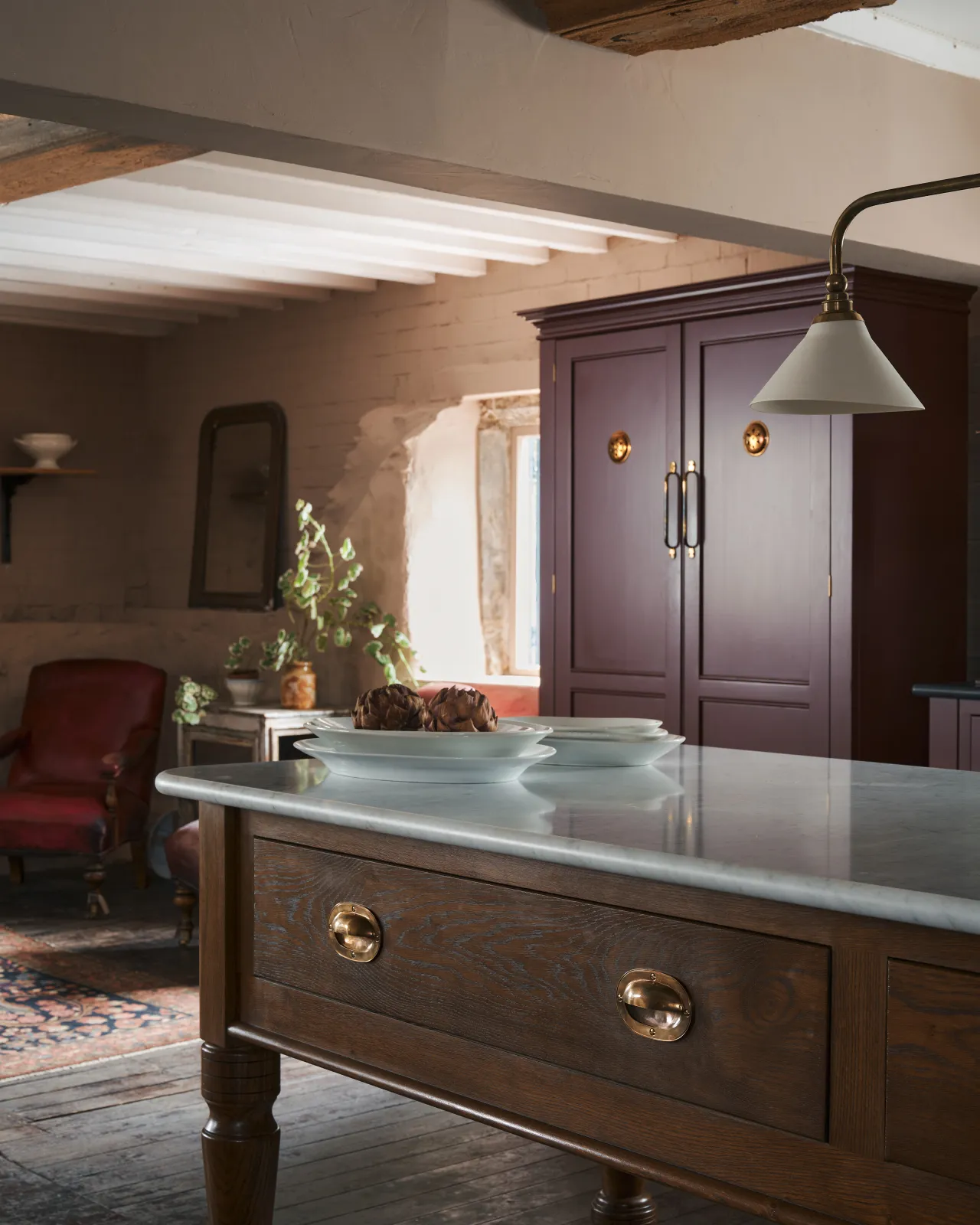 An oblique view of a large Victorian-inspired prep table with a Carrara marble worktop, a dark oak stained frame and turned legs and two oval-shaped cup handles with an authentic and warm burnished brass finish.