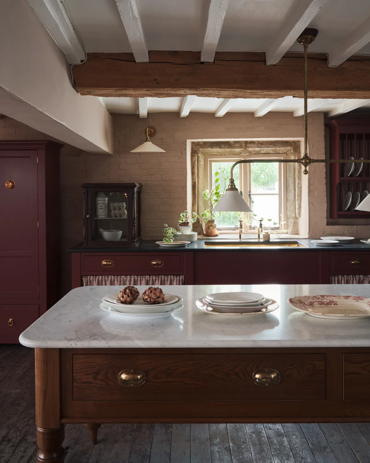 A straight-on view of a large Victorian-inspired prep table with a Carrara marble worktop, a dark oak stained frame and turned legs and two oval-shaped cup handles with an authentic and warm burnished brass finish.