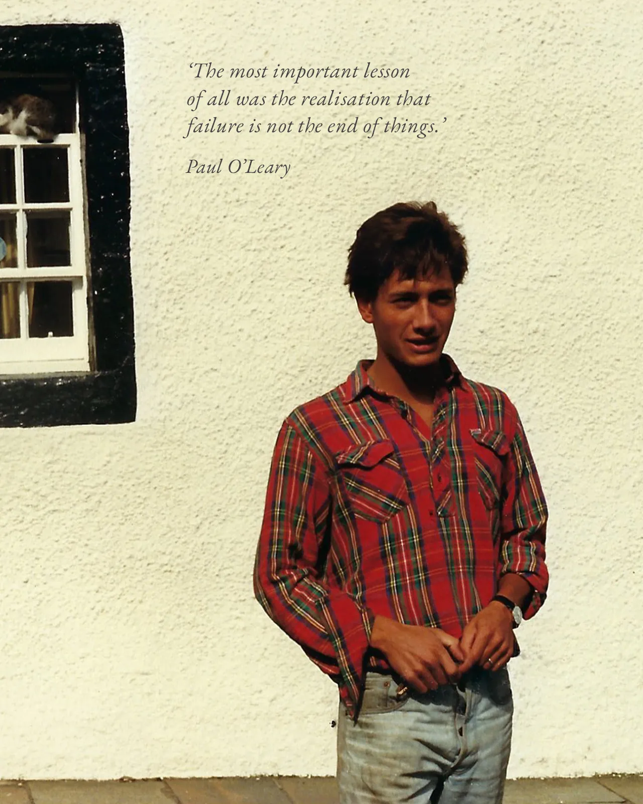 A photo of a young Paul O'Leary, wearing a red plaid shirt in front of a rendered cottage, with the quote "The most important lesson of all was the realisation that failure is not the end of things."