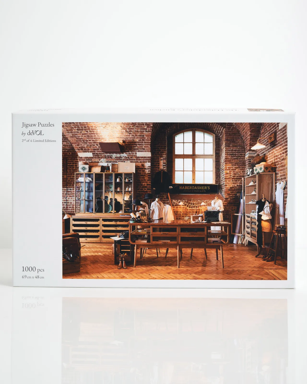A white jigsaw puzzle box with a photo of a mid-century-style oak kitchen in a red brick room with warm parquet wood flooring. The box features the text, 'Jigsaw Puzzles by deVOL, 2 of 6 Limited Edition. 1000pcs, 69 x 48 cm'.