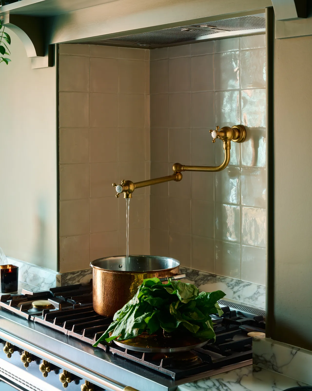 An oblique view of a traditional-style aged brass pot filler tap fitted in a small alcove above a vintage copper pan.
