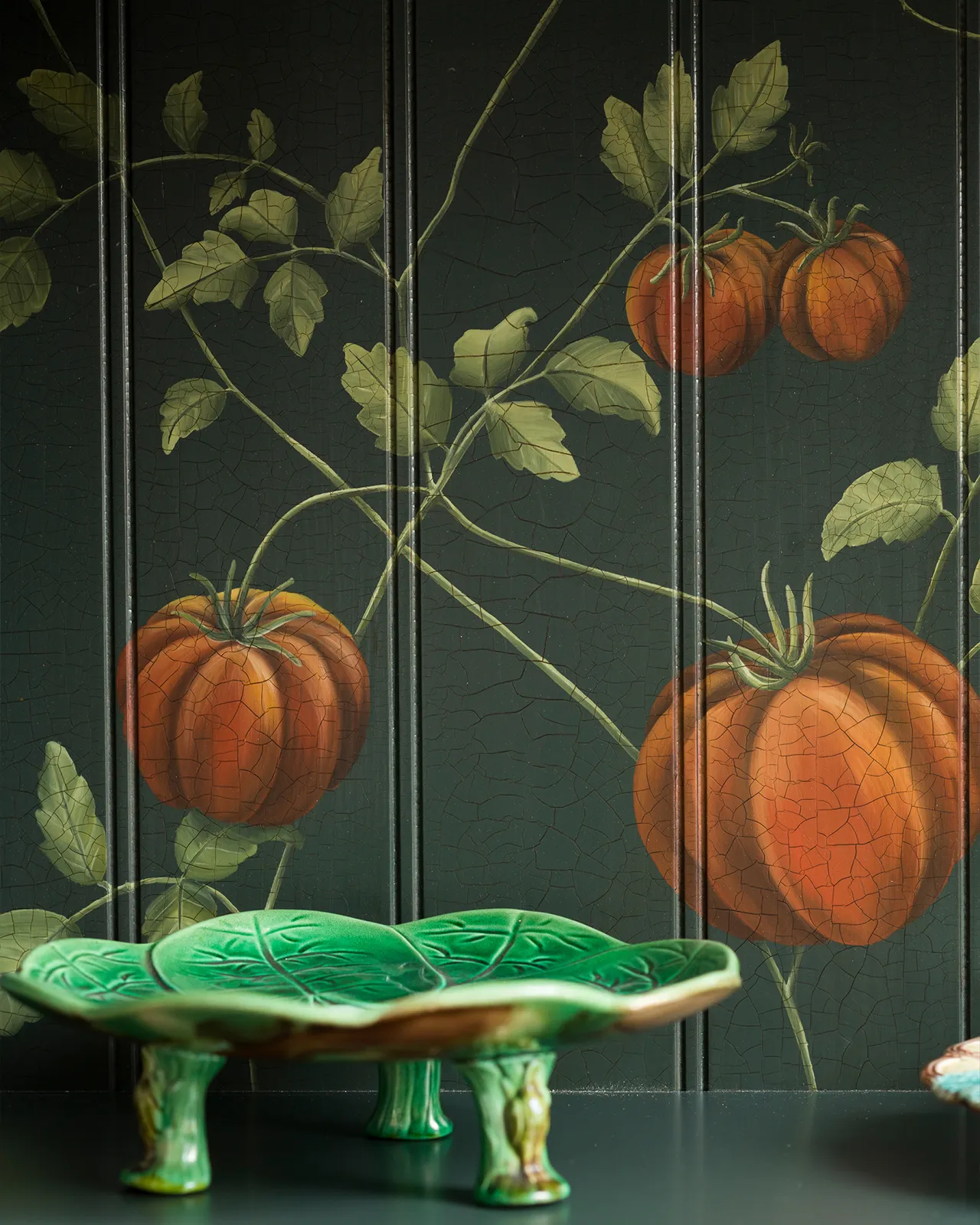 A close-up view of painted heirloom tomatoes on a dark green tongue and groove back panel.