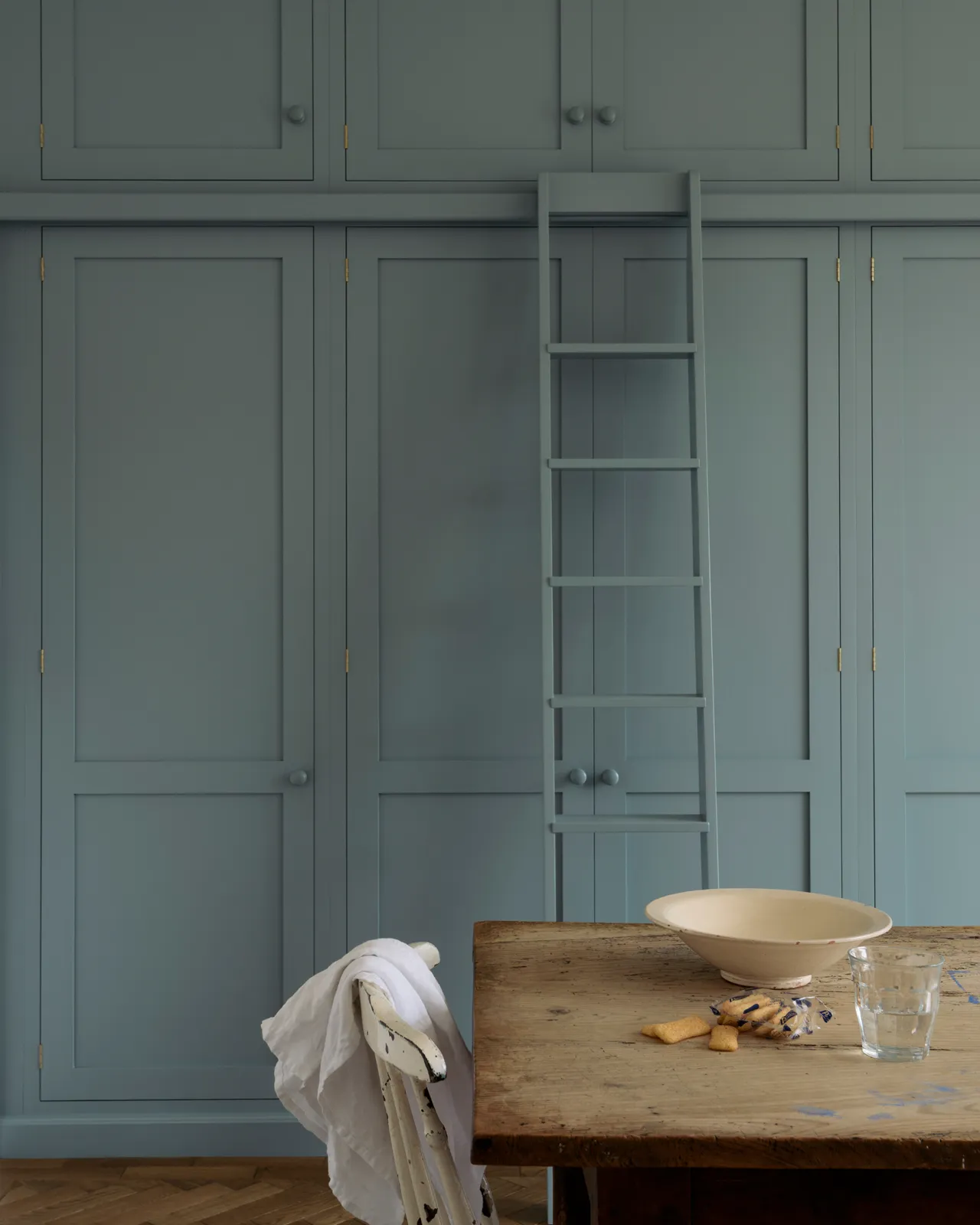 A straight-on view of a tall bank of duck-egg blue painted Shaker-style pantry cupboards with a sliding ladder.