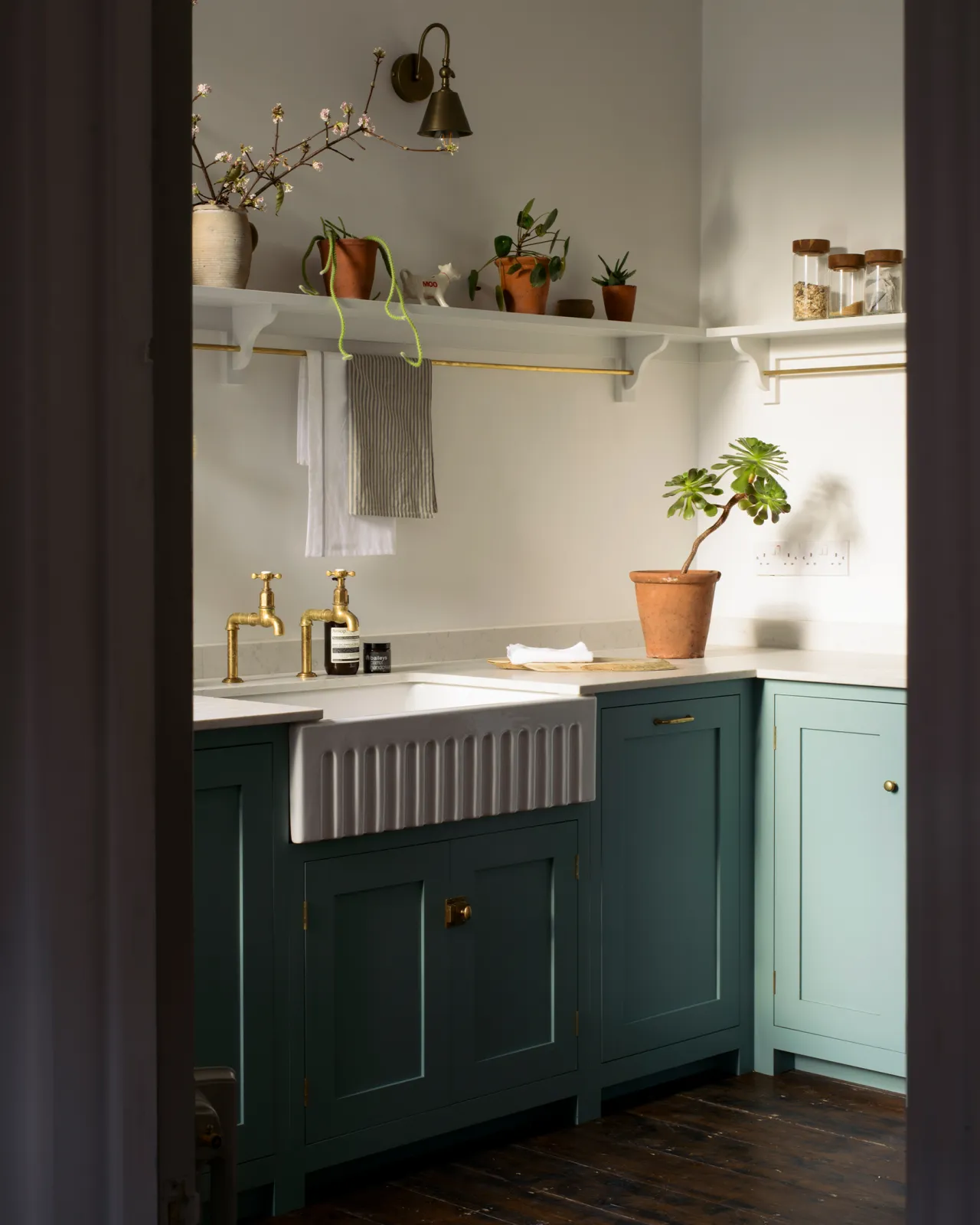 Looking through a doorway at a simple duck-egg blue painted Shaker-style kitchen with a fluted Belfast sink and white walls.