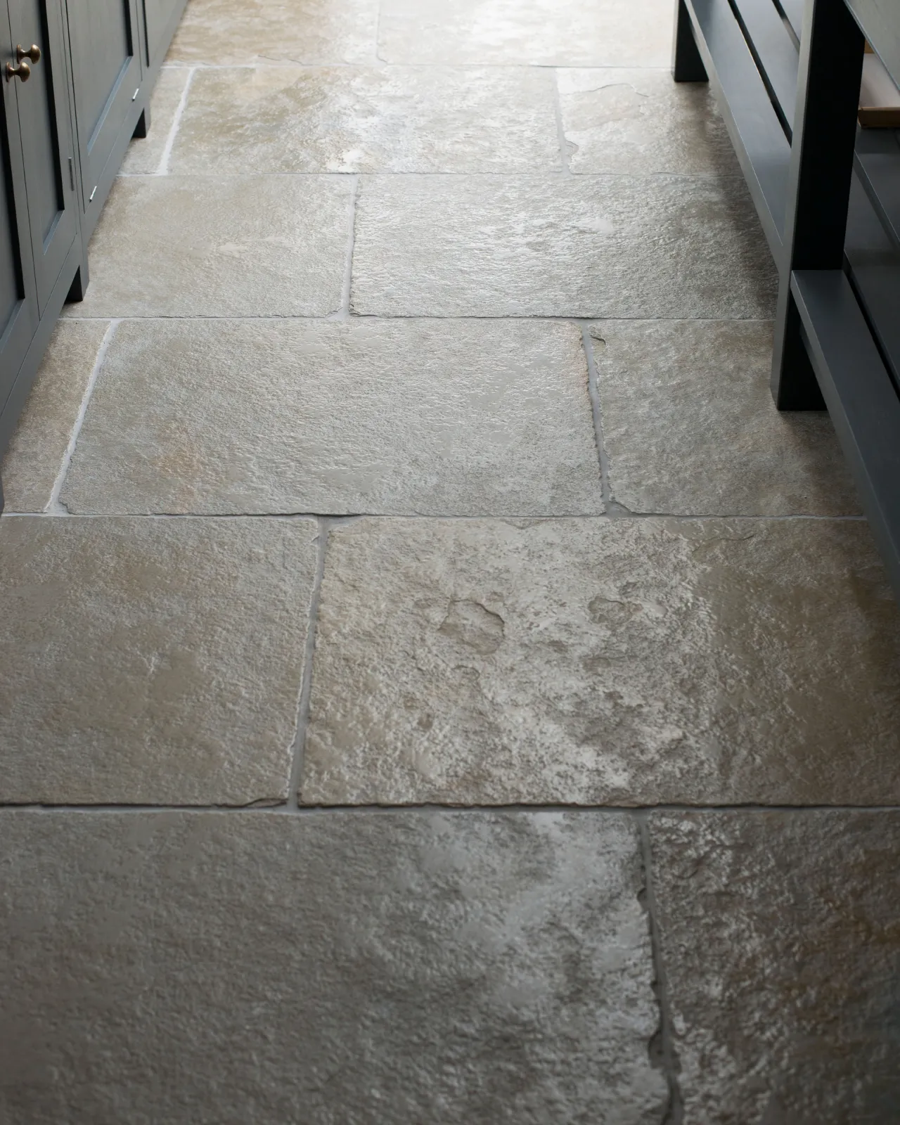 Light reflecting off the smooth worn surface of an aged limestone floor with natural earthy tones of green, brown and grey.