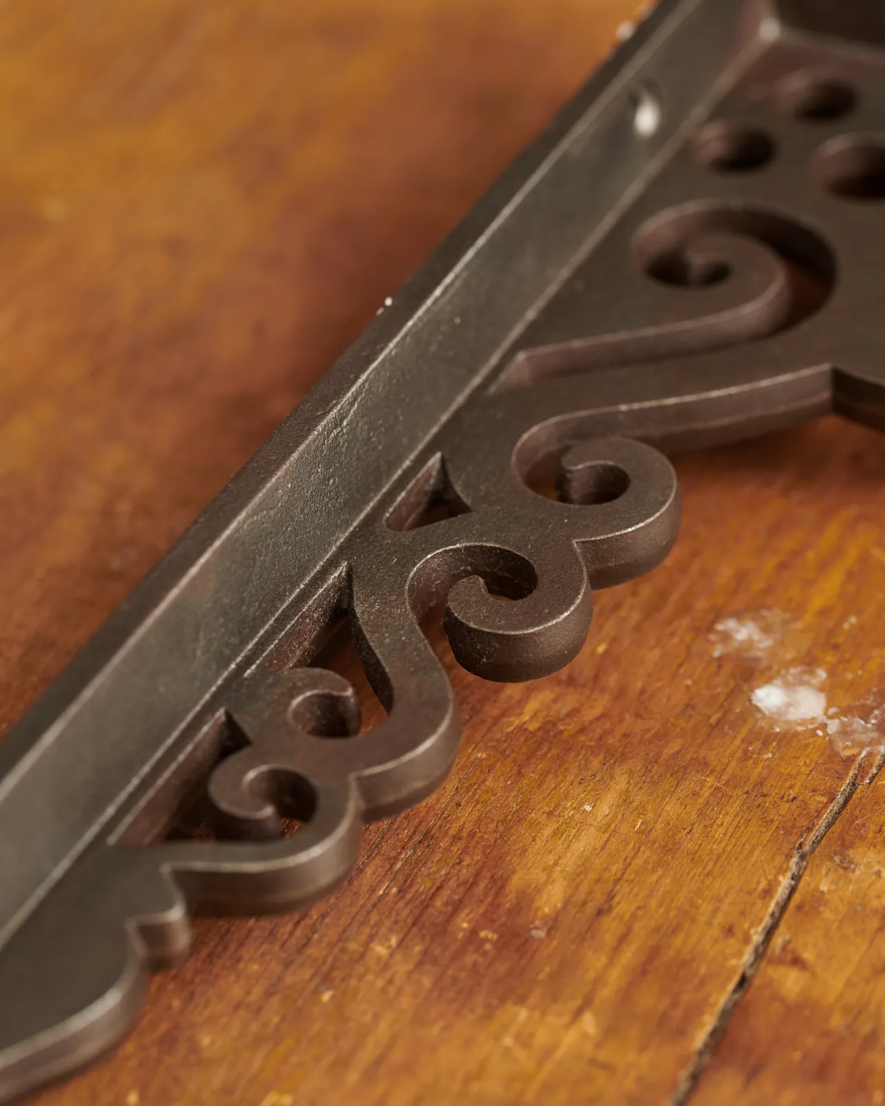 A close-up view of the decorative cutout patterns on a large Victorian-inspired ornate cast iron shelf bracket.