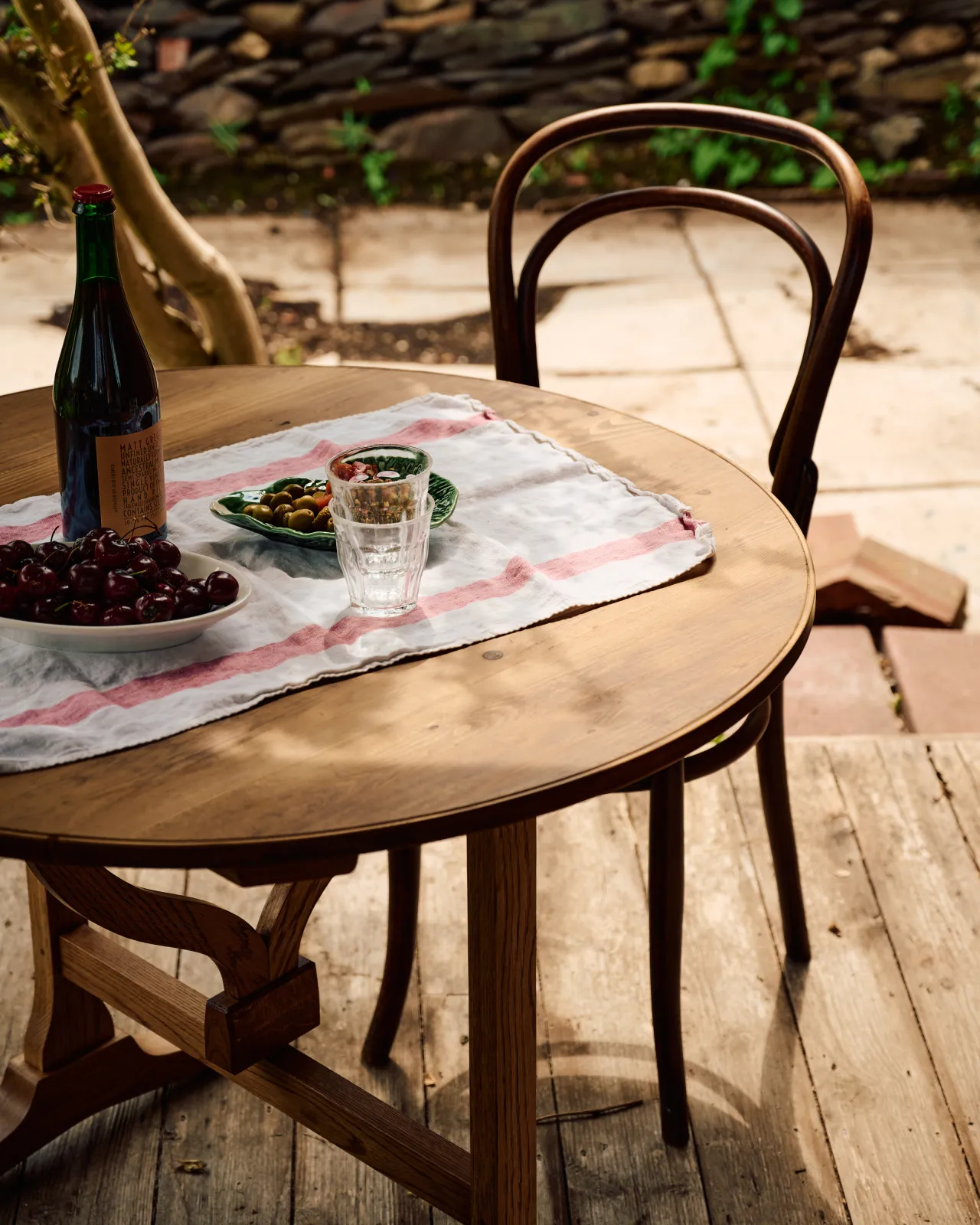 A close-up view of a small round pine dining table and a vintage café-style chair outdoors on wooden decking.
