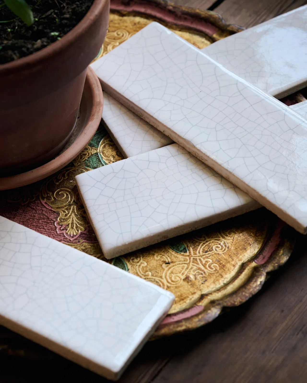 Several white glossy metro tiles on a decorative brass plate, each tile has unique delicate crazing across the surface.