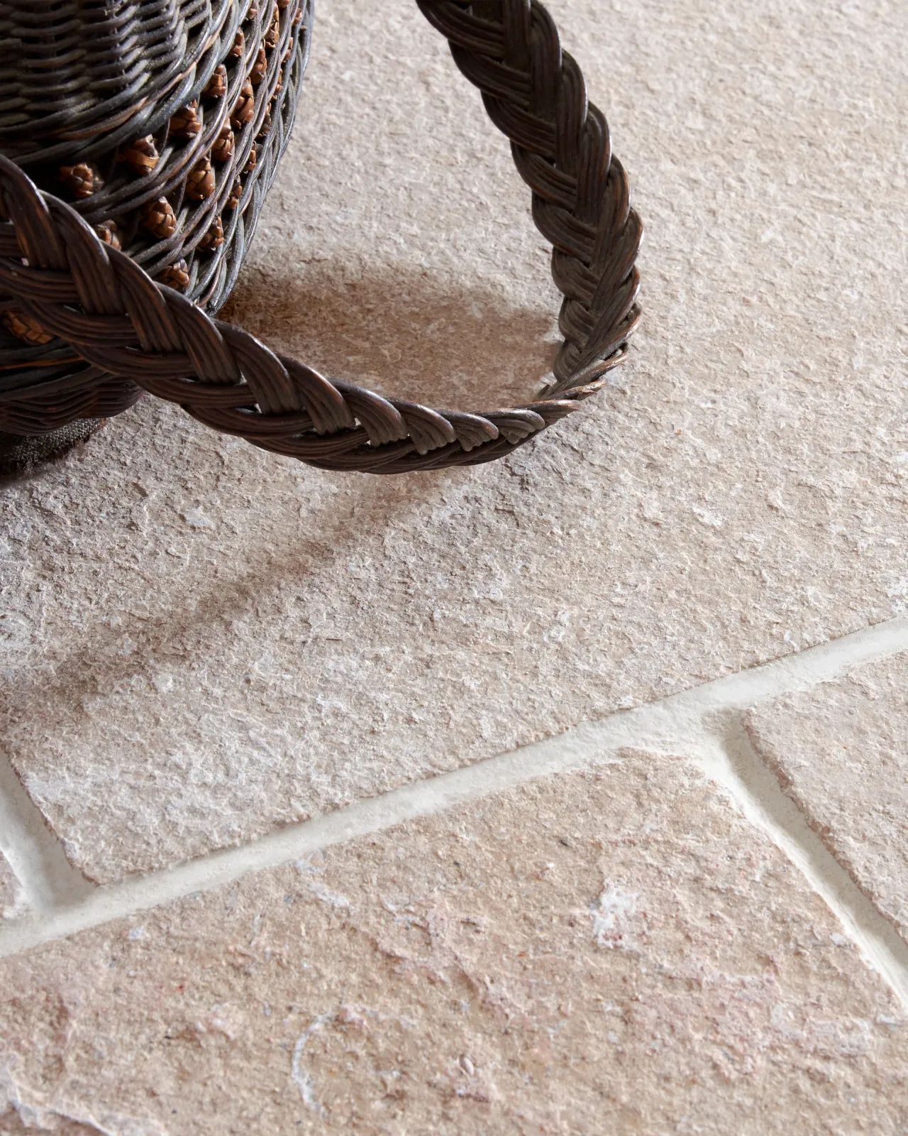 A close-up oblique view of a wicker basket on a soft creamy pink coloured limestone floor with a lightly textured surface.