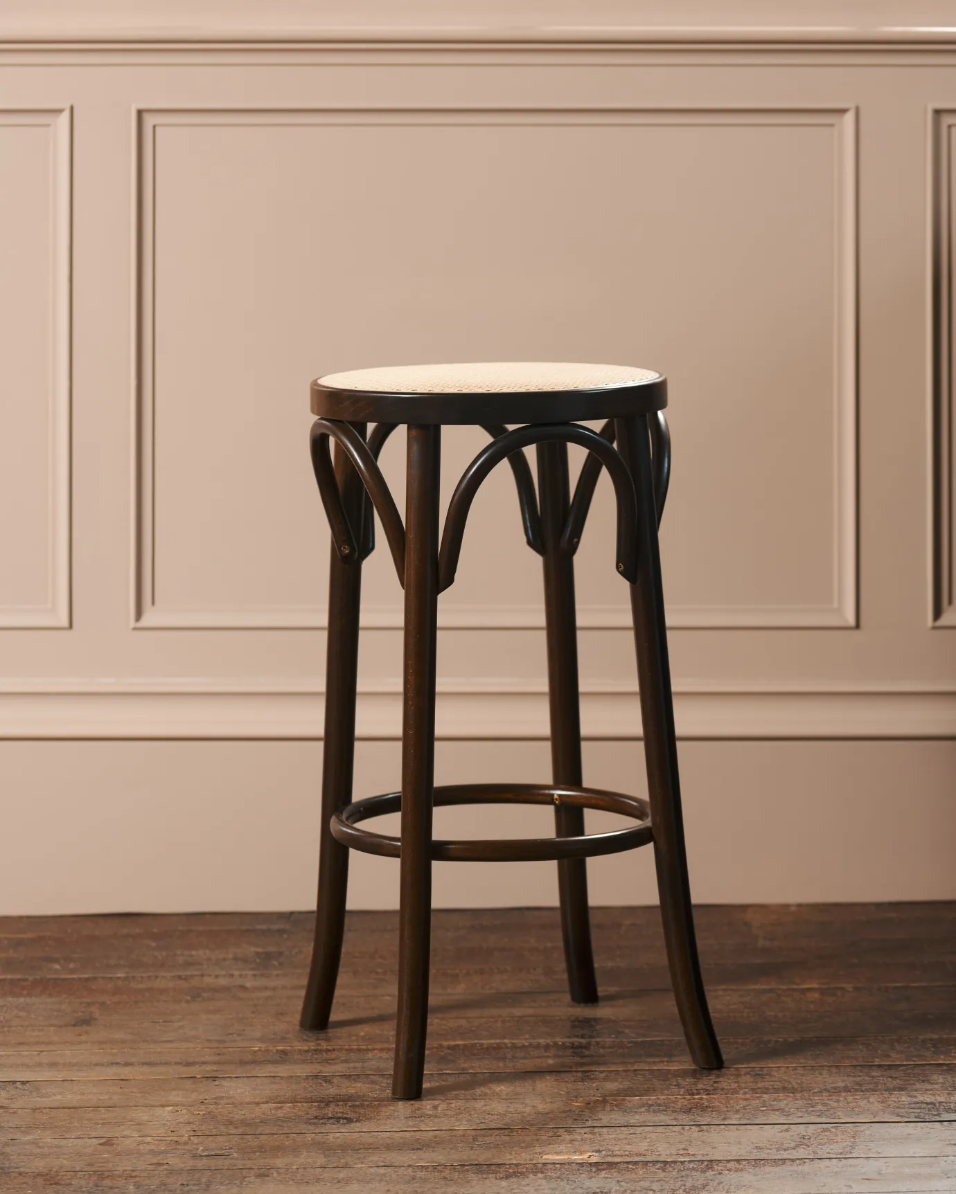 A three-quarters profile view of a café-style bar stool with a dark stained frame and light woven ratten seat.
