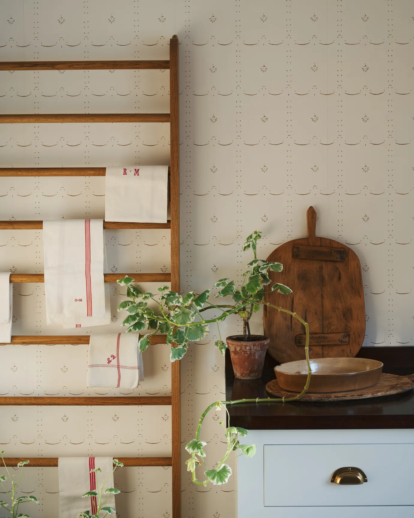 A delicately patterned wallpaper behind a mid-century-style oak hanging rack.